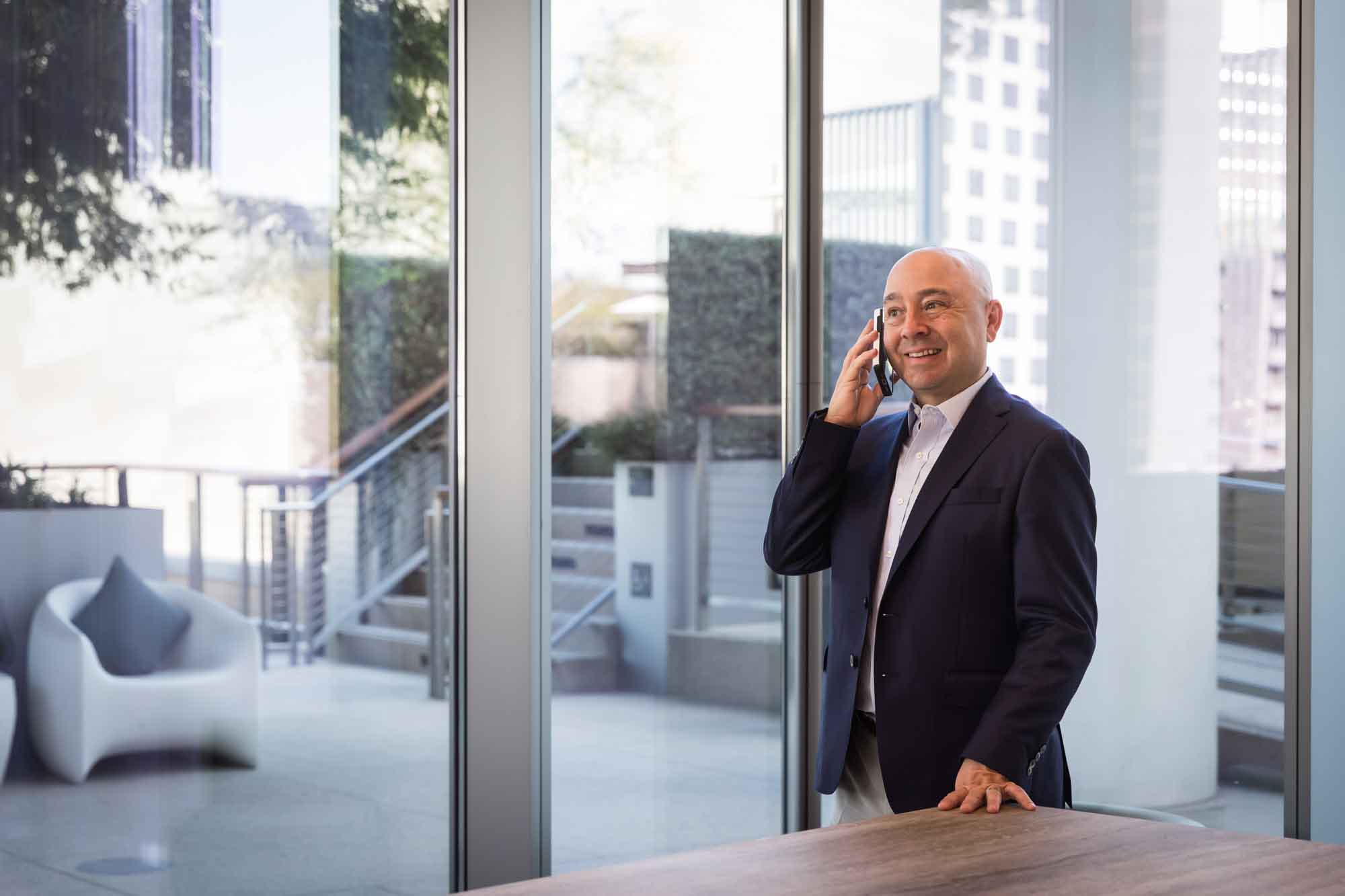 Executive portrait of businessman wearing blue jacket and khaki pants talking on phone in front of window with patio in background for an article on how to prepare for a branding photo shoot