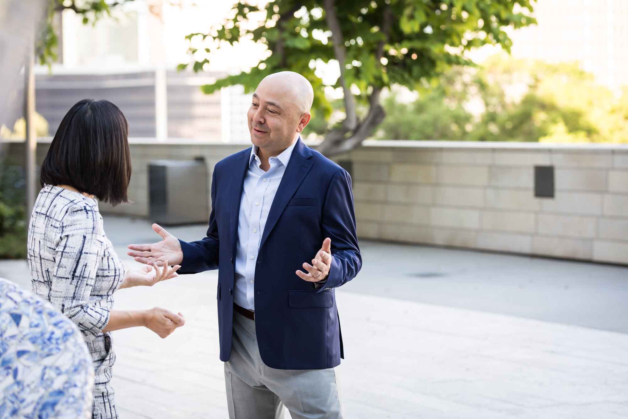 Businessman wearing blue jacket and khaki pants walking and talking with Asian American female colleague wearing dress in Blue Ribbon Garden for an article on how to prepare for a branding photo shoot