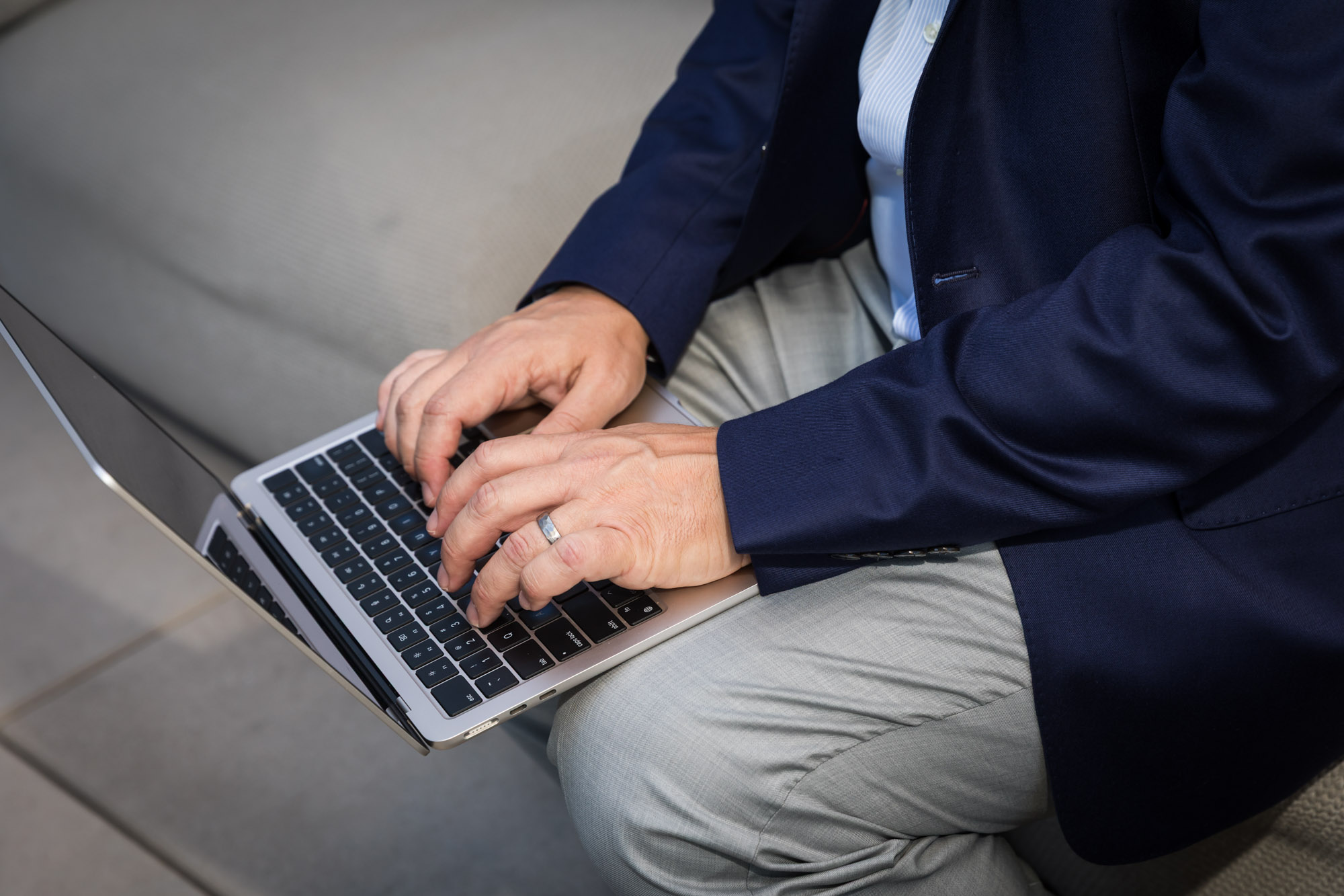 Close up of man wearing blue blazer typing on laptop for an article on how to prepare for a branding photo shoot
