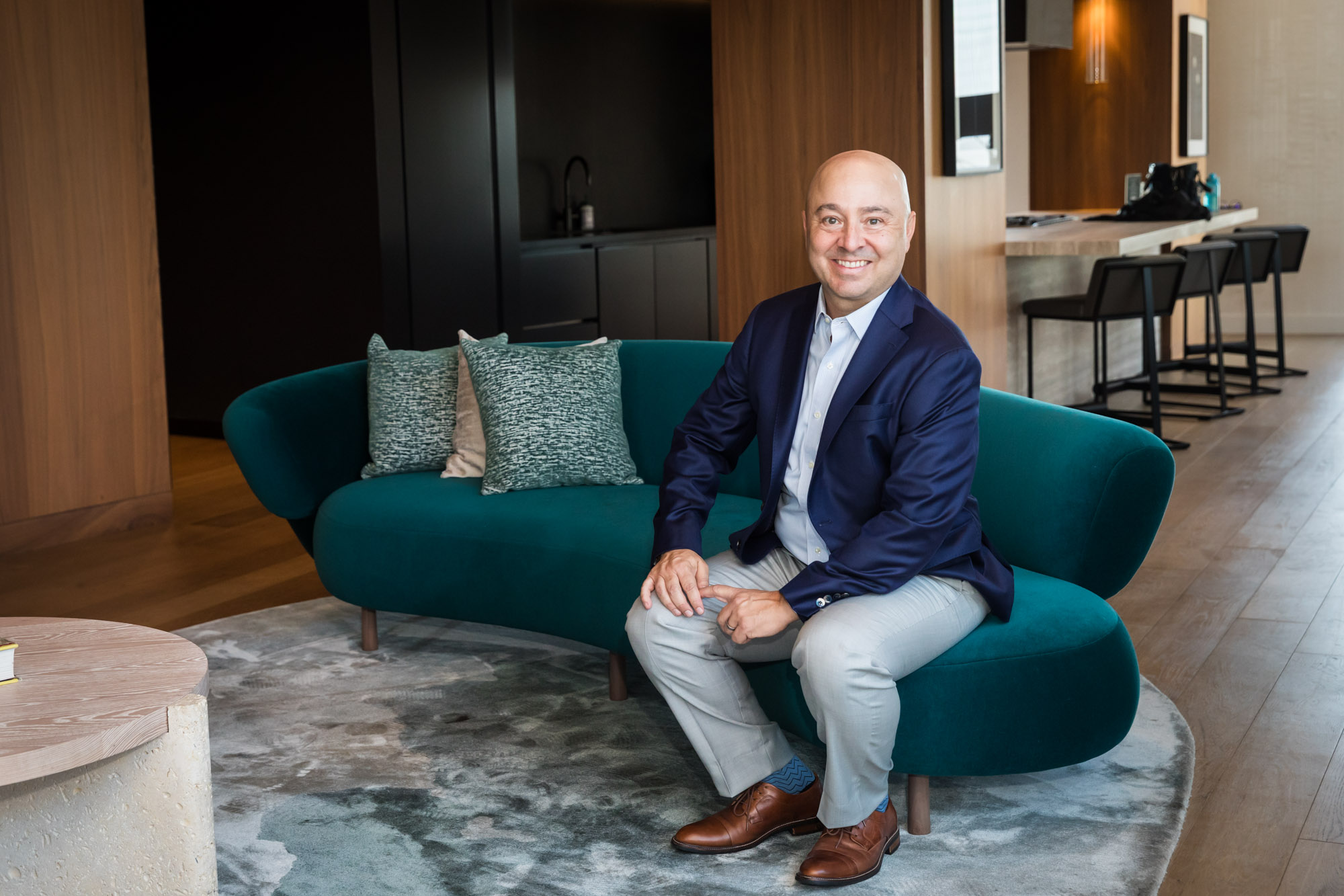 Executive portrait of businessman wearing blue blazer and blue and white shirt seated on teal couch for an article on how to prepare for a branding photo shoot