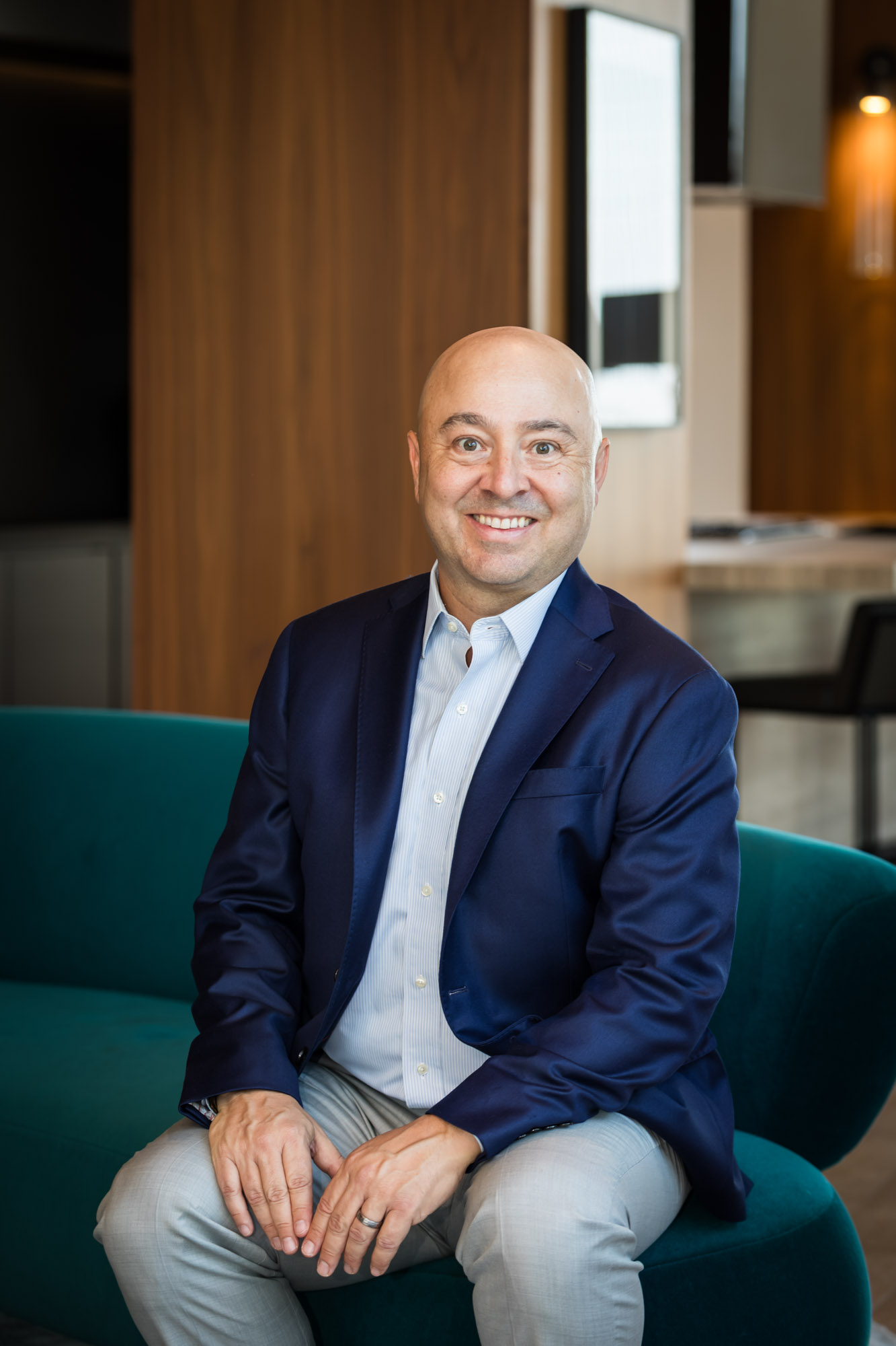 Executive portrait of businessman wearing blue blazer and blue and white shirt seated on teal couch for an article on how to prepare for a branding photo shoot