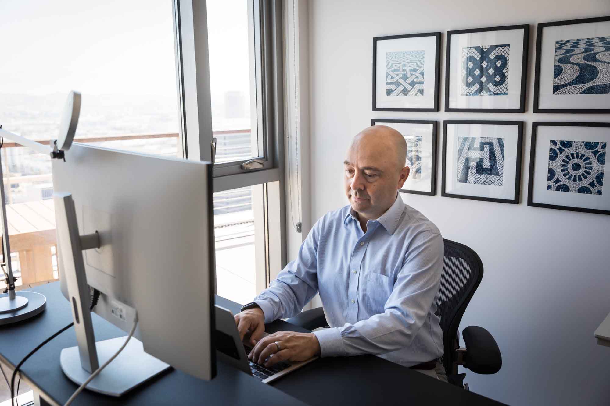 Businessman wearing white and blue shirt seated and in front of a computer in a home office for an article on how to prepare for a branding photo shoot