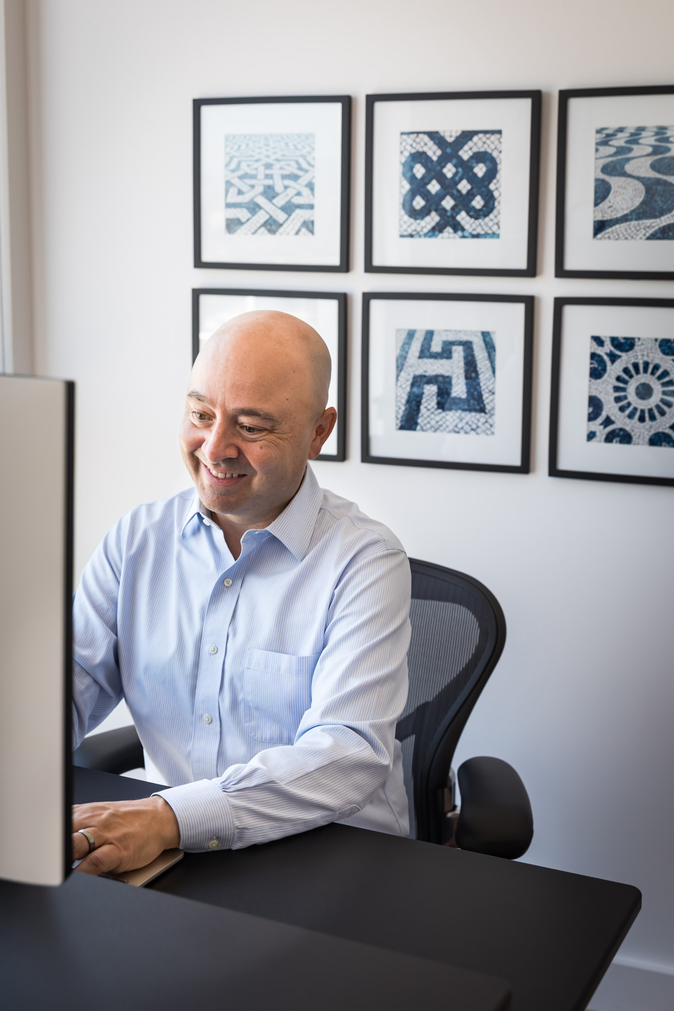 Businessman wearing white and blue shirt seated and in front of a computer in a home office for an article on how to prepare for a branding photo shoot