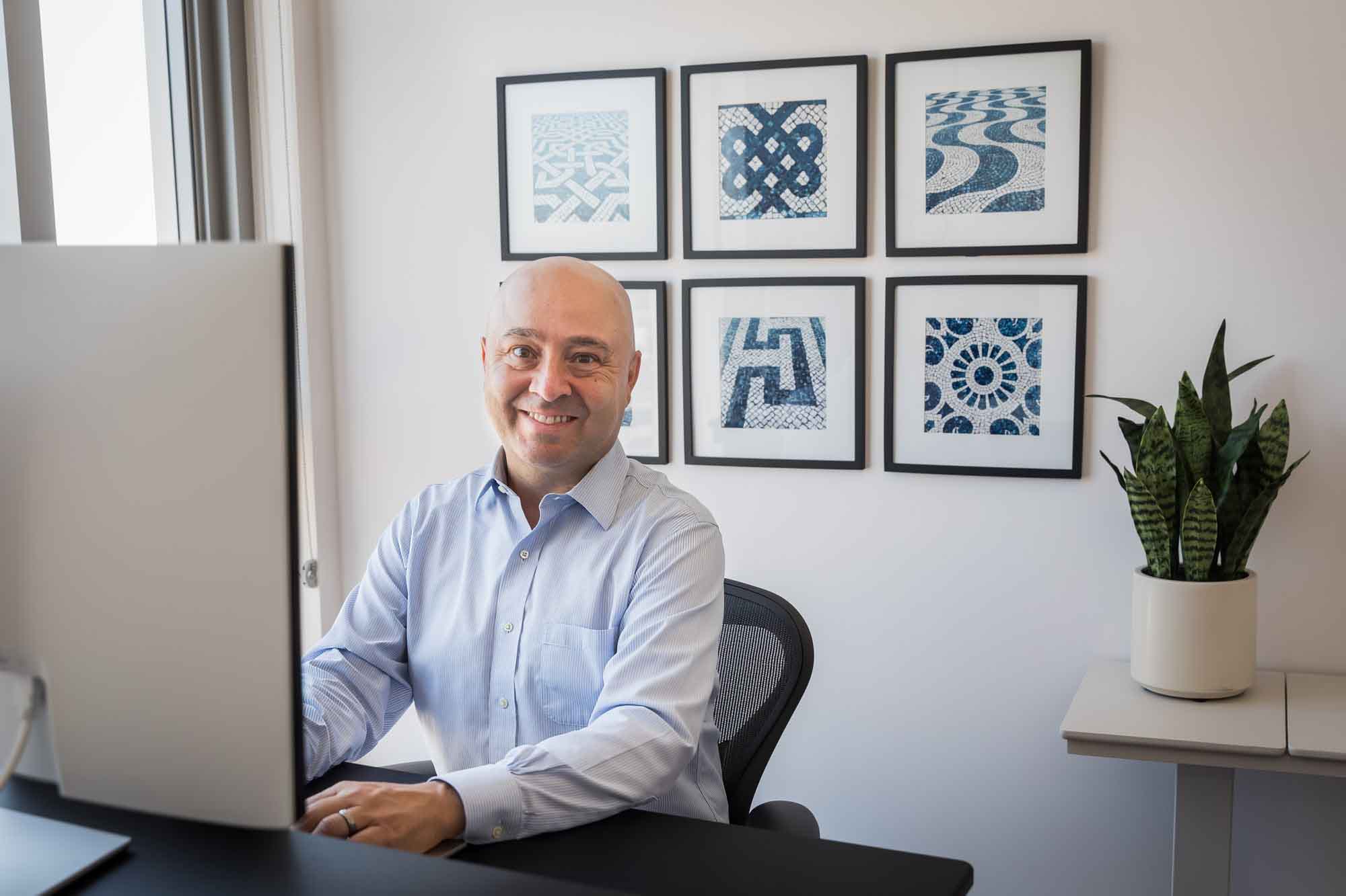 Businessman wearing white and blue shirt seated and in front of a computer in a home office for an article on how to prepare for a branding photo shoot