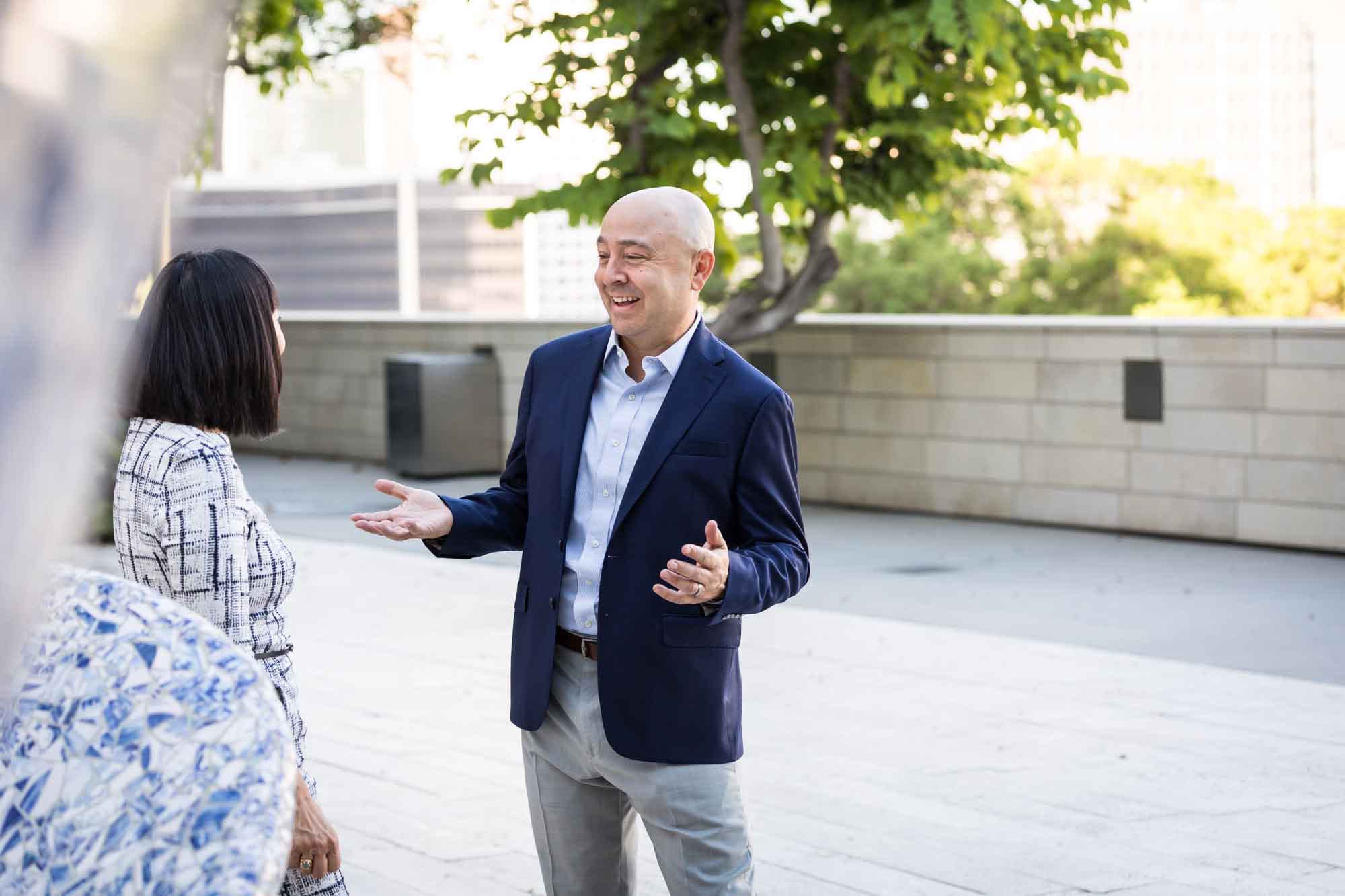 Businessman wearing blue jacket and khaki pants walking and talking with Asian American female colleague wearing dress in Blue Ribbon Garden for an article on how to prepare for a branding photo shoot
