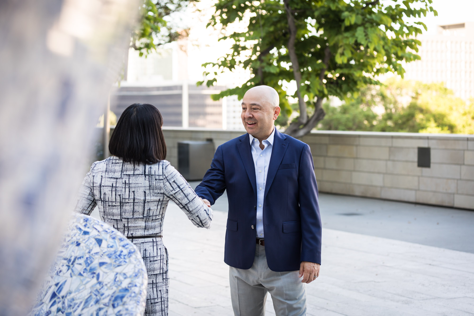 Businessman wearing blue jacket and khaki pants walking and talking with Asian American female colleague wearing dress in Blue Ribbon Garden for an article on how to prepare for a branding photo shoot