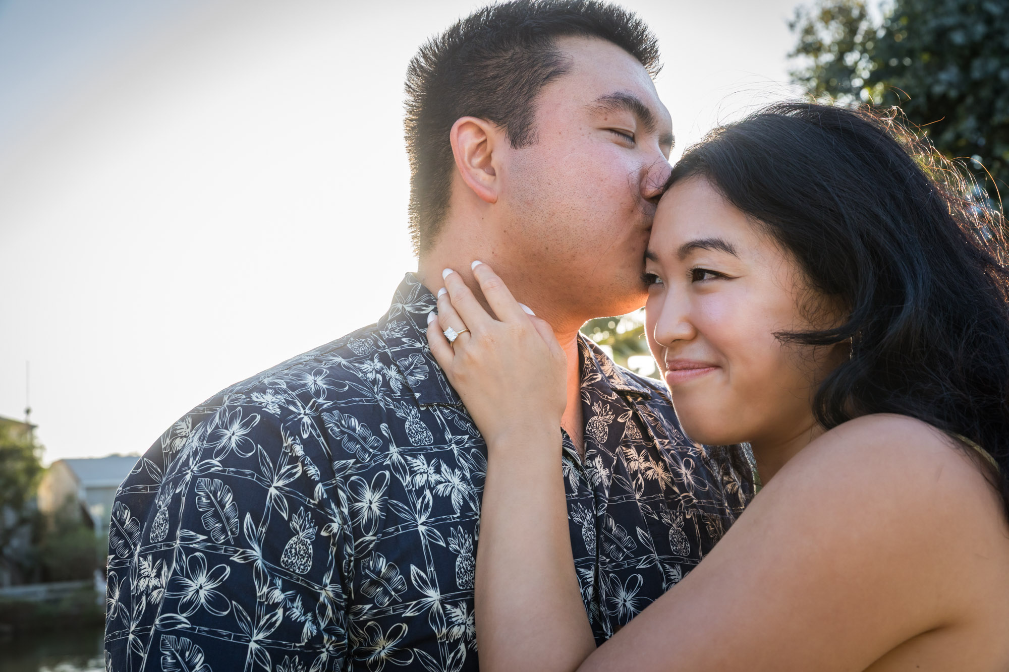 Man wearing blue and white patterned shirt and sunglasses and woman wearing sleeveless yellow dress and sunglasses in front of Surf Shop during a Venice Canals engagement photo shoot