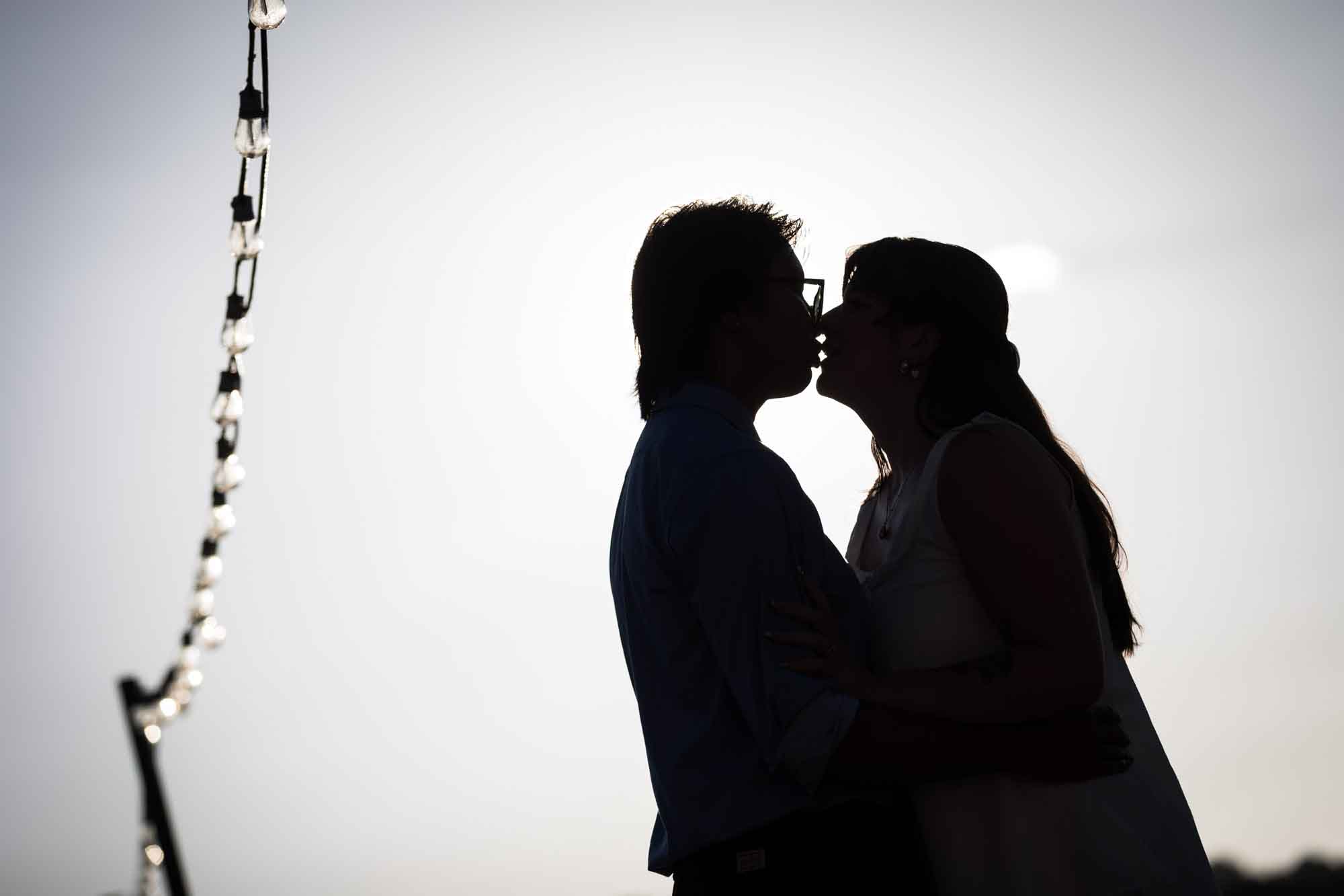 Silhouette shot of man and woman kissing with string of lights to the left of frame