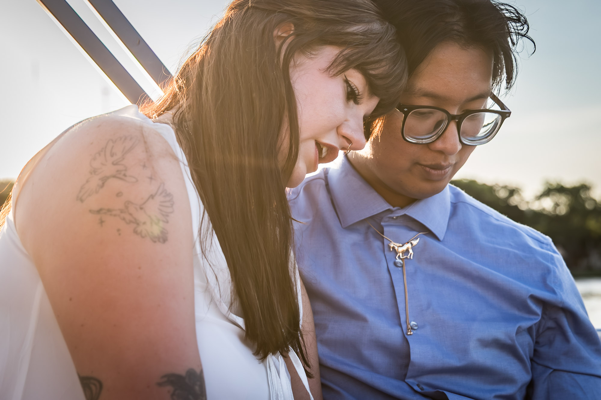 Man wearing blue shirt sitting to the right of woman wearing sleeveless, white dress on a boat with lake in the background