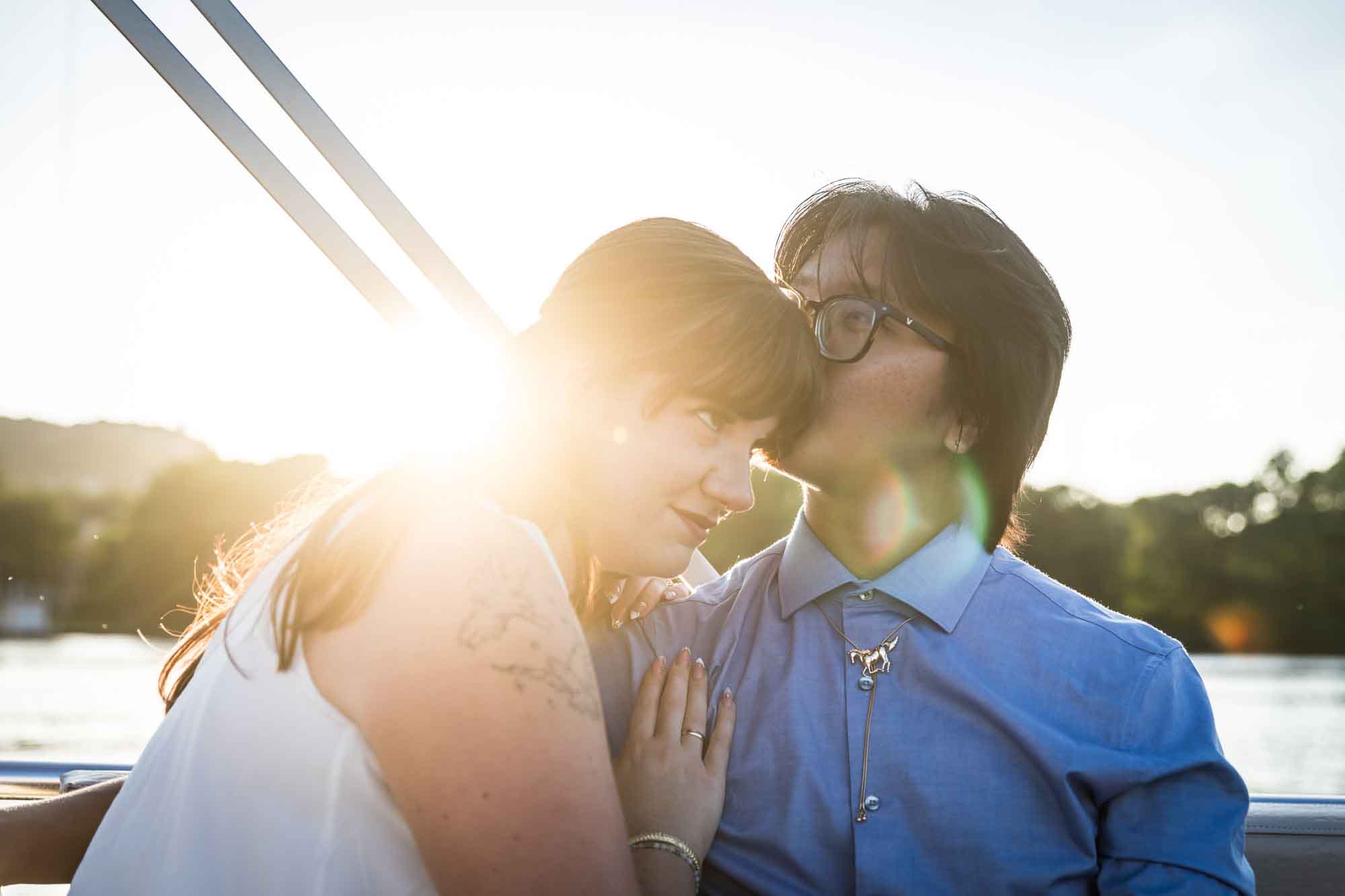 Man wearing blue shirt kissing woman wearing sleeveless, white dress on a boat with lake in the background