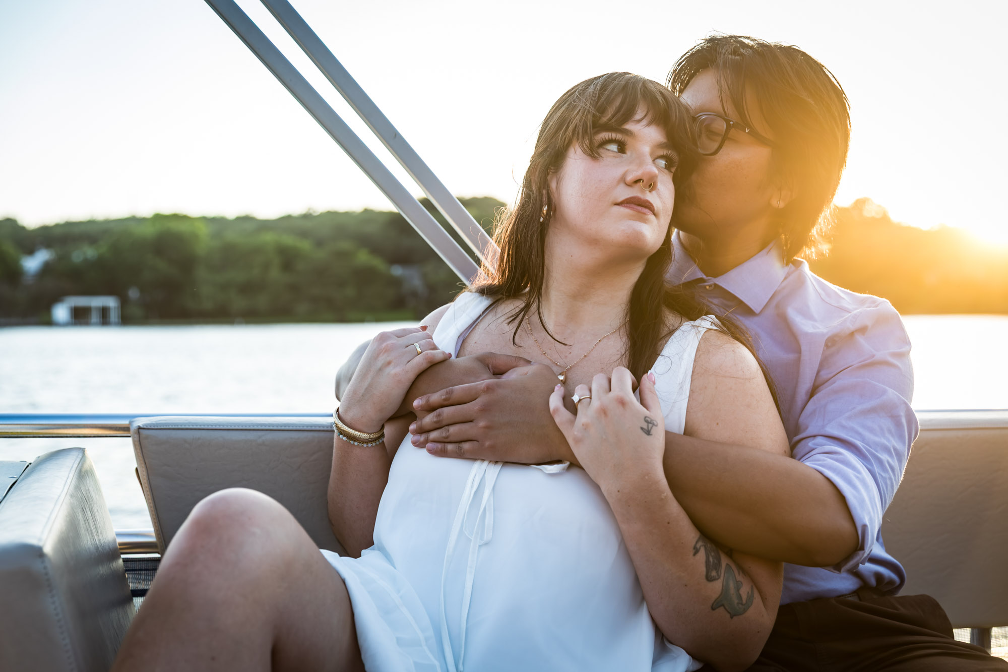 Man wearing blue shirt hugging woman wearing sleeveless, white dress on a boat with lake in the background
