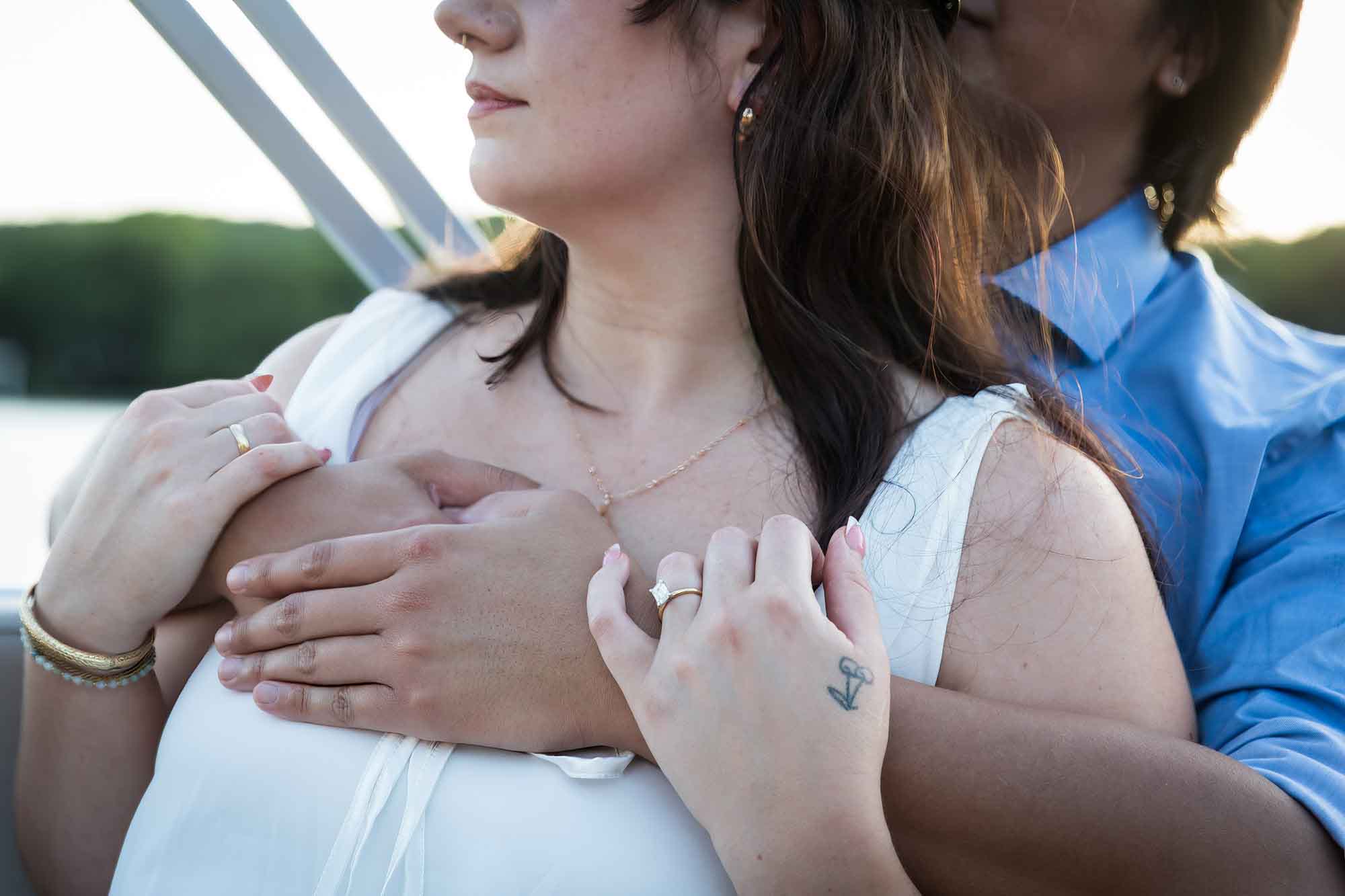 Close up of man wearing blue shirt hugging woman wearing sleeveless, white dress on a boat with lake in the background