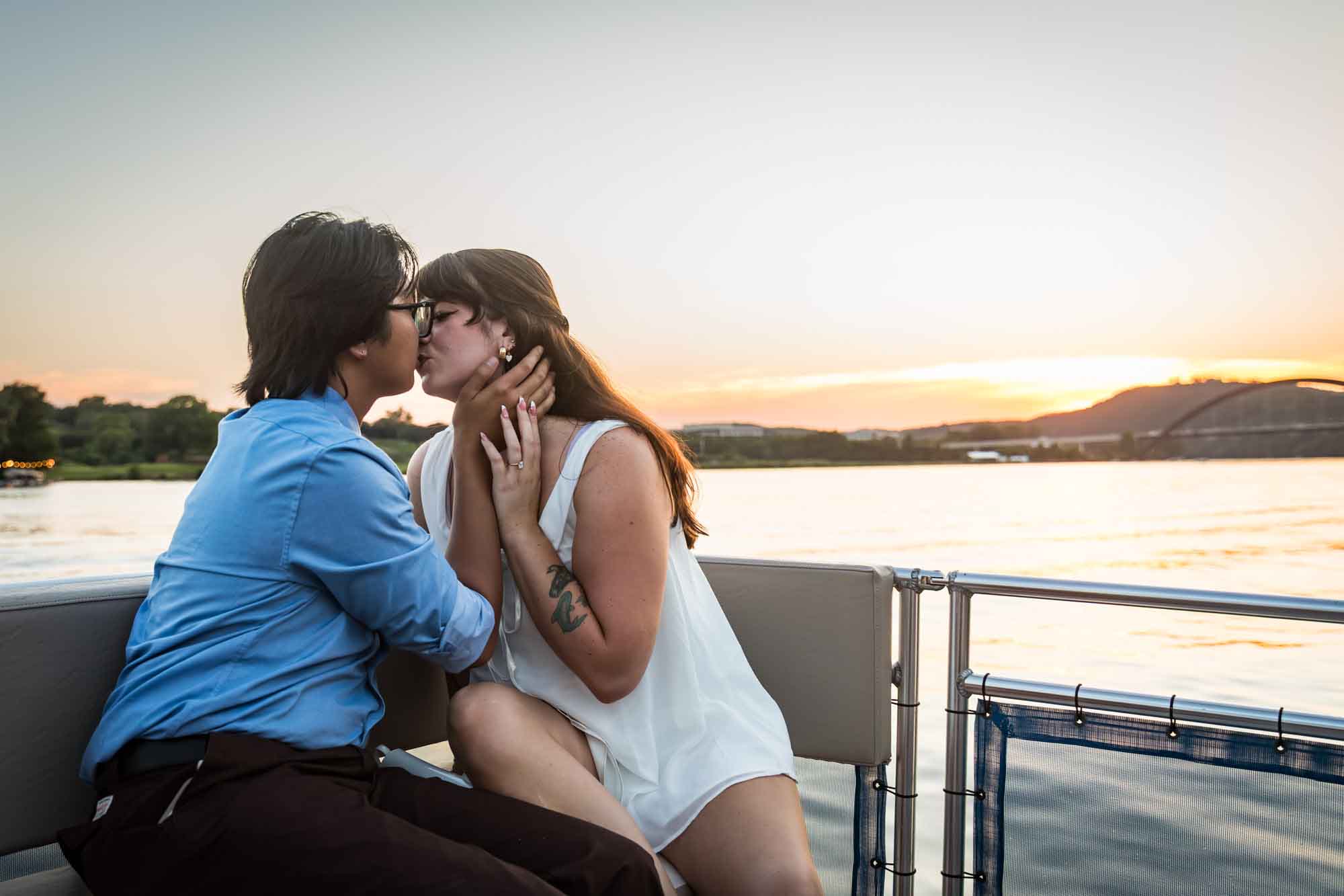 Man wearing blue shirt kissing woman wearing sleeveless, white dress on a boat with lake in the background