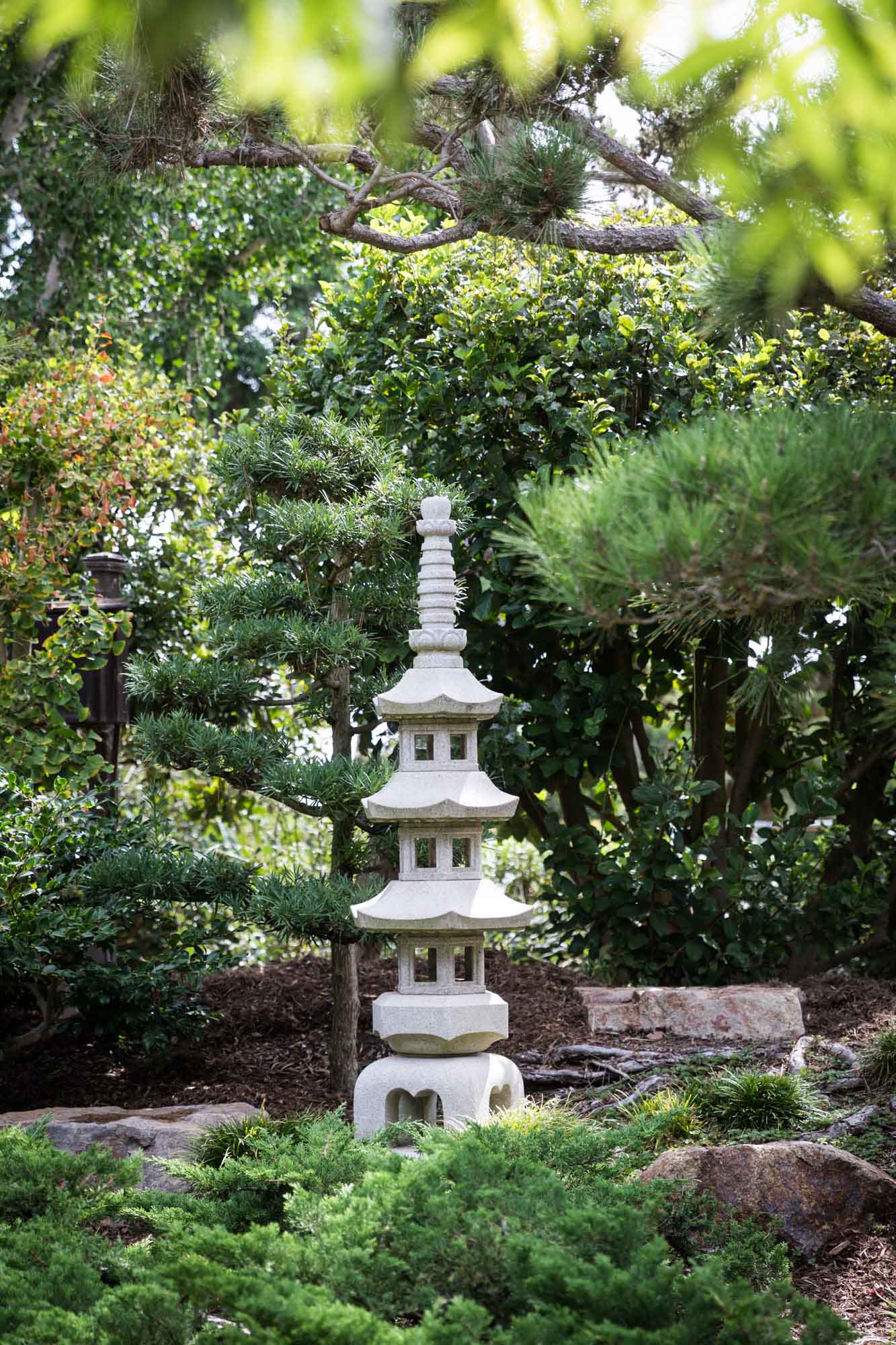 Tall stone pagoda in front of trees and bushes in Earl Burns Miller Japanese Garden for an article on where to propose in Long Beach