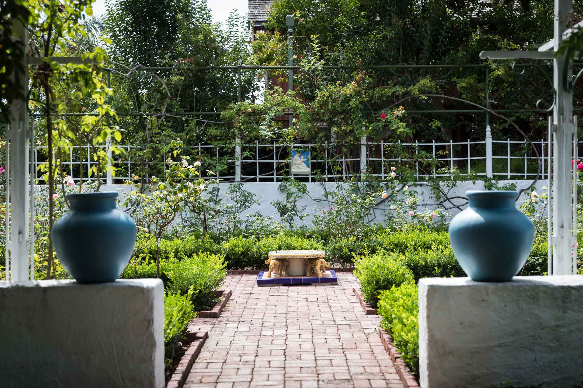 A brick pathway with two blue urns sitting on concrete walls on either side in the rose garden at Rancho Los Alamitos for an article on where to propose in Long Beach