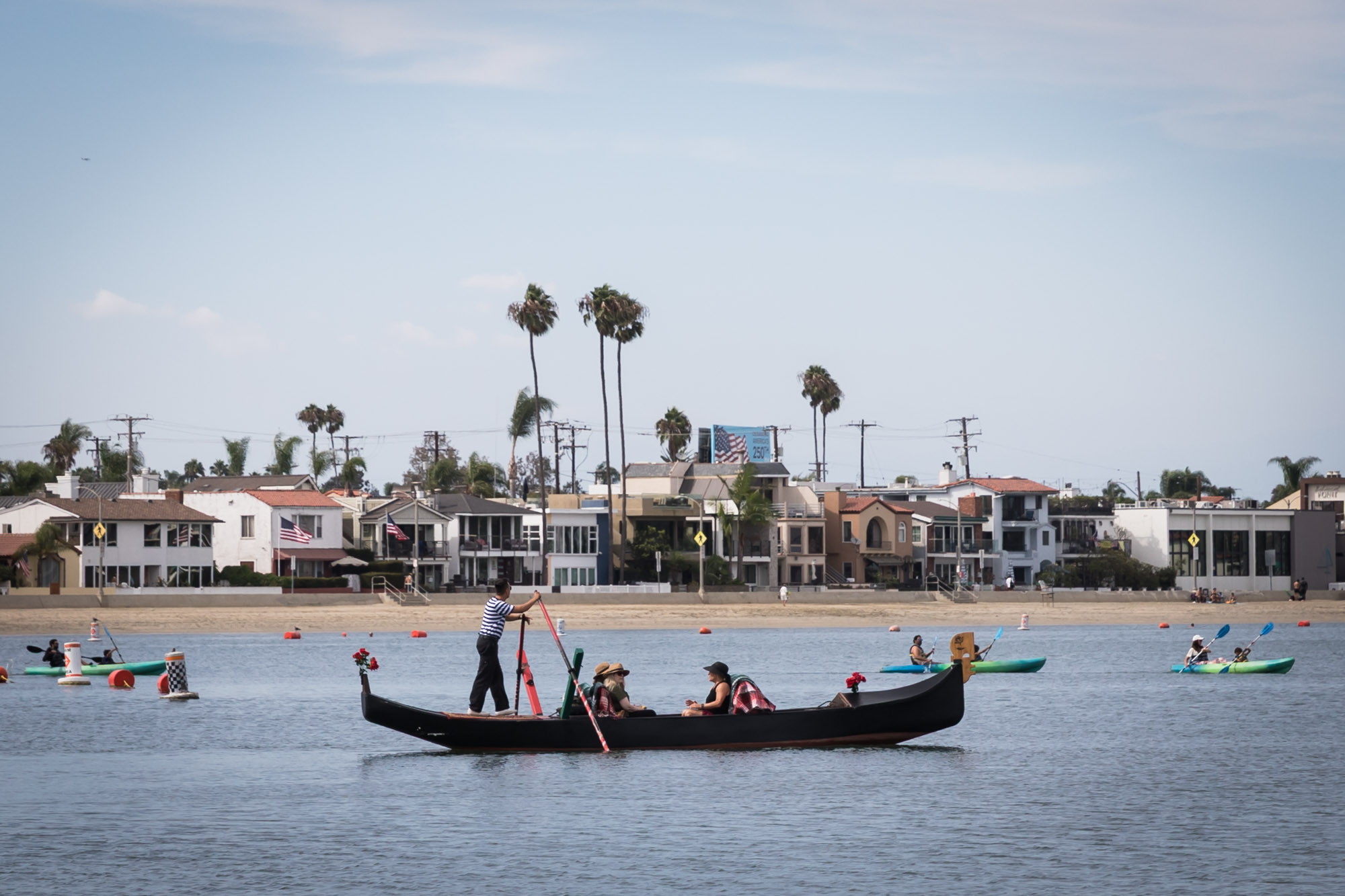 A gondolier driving a gondola in front of waterfront homes for an article on where to propose in Long Beach