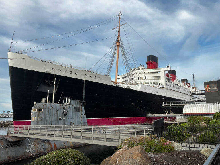 The Queen Mary and a submarine viewed from land with clouds overhead for an article on where to propose in Long Beach