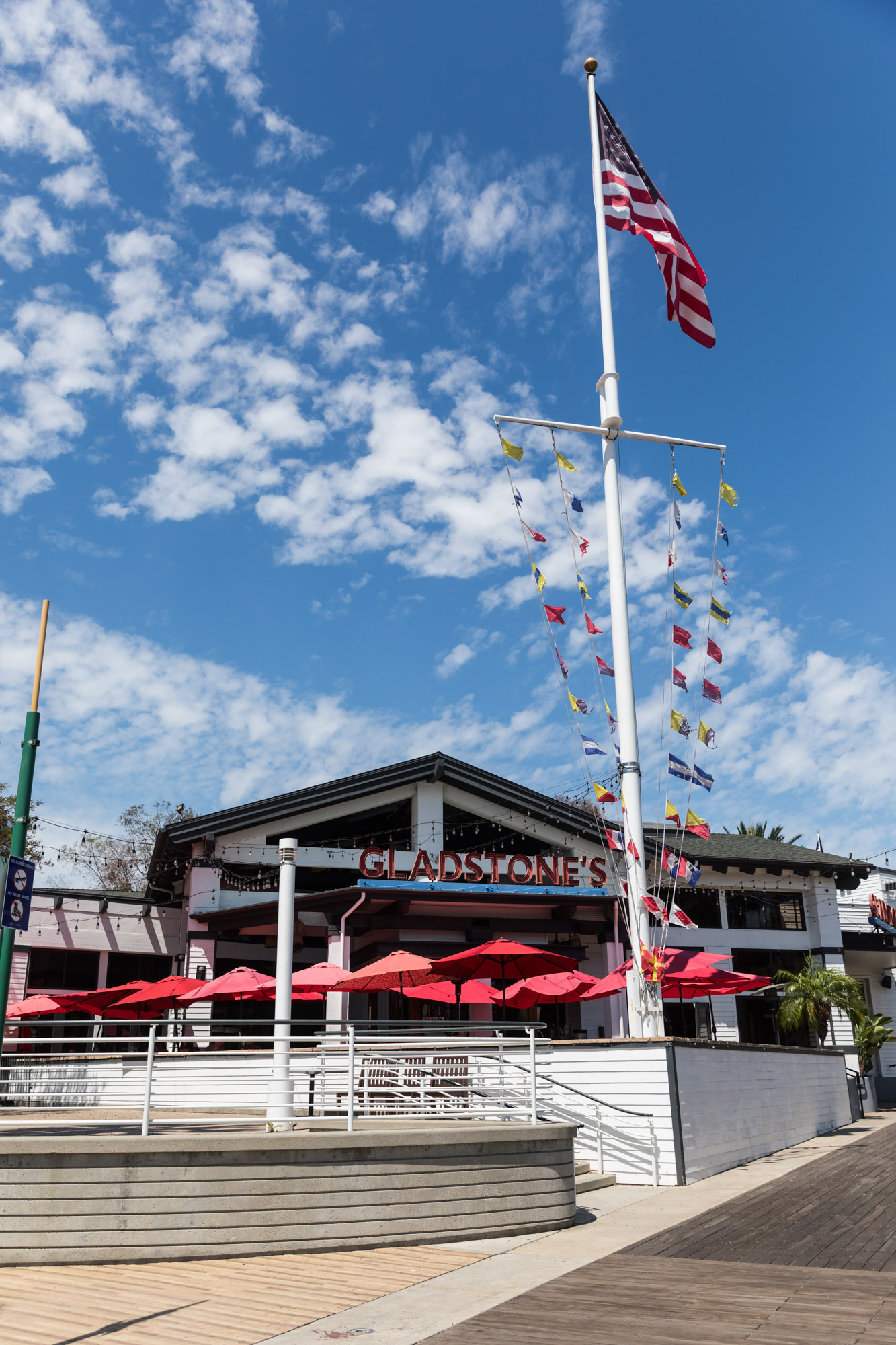 The exterior of Gladstone's Restaurant Long Beach with a flag pole in front with the American flag and naval flags flying for an article on where to propose in Long Beach