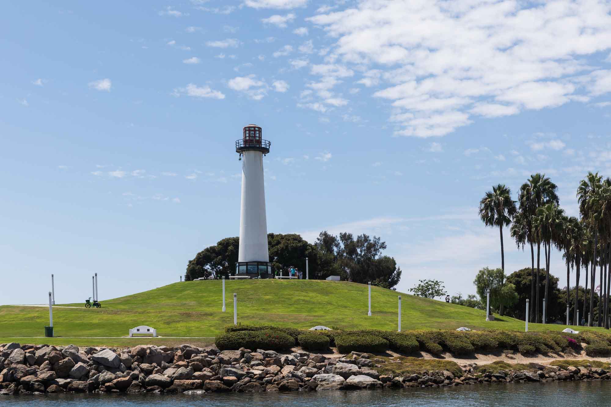The Lions Lighthouse on a grassy hill with a rock jetty in front of the water at Shoreline Aquatic Park for an article on where to propose in Long Beach