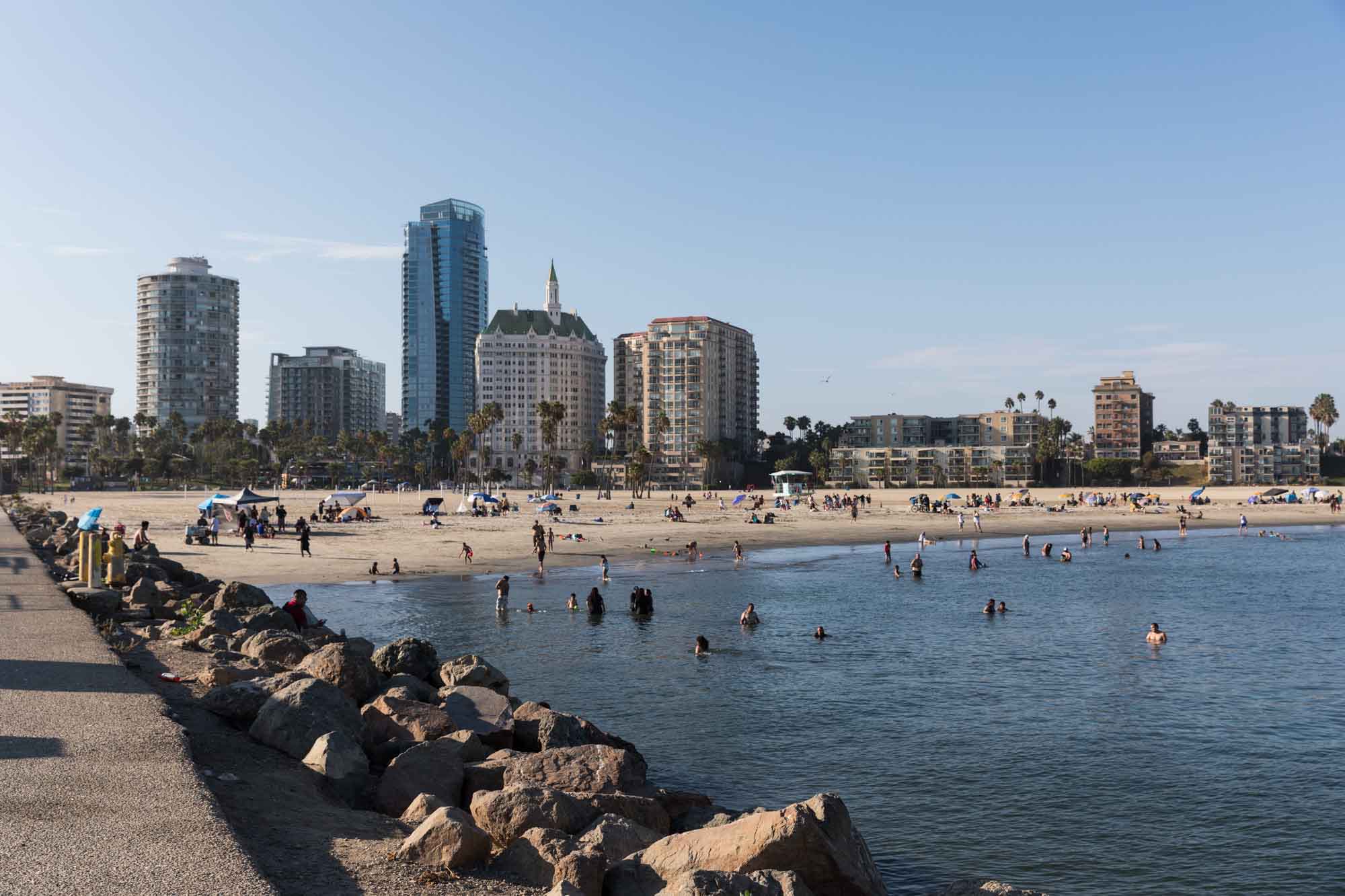 People swimming at Alamitos Beach with rock jetty on the left and Long Beach skyline in the background for an article on where to propose in Long Beach