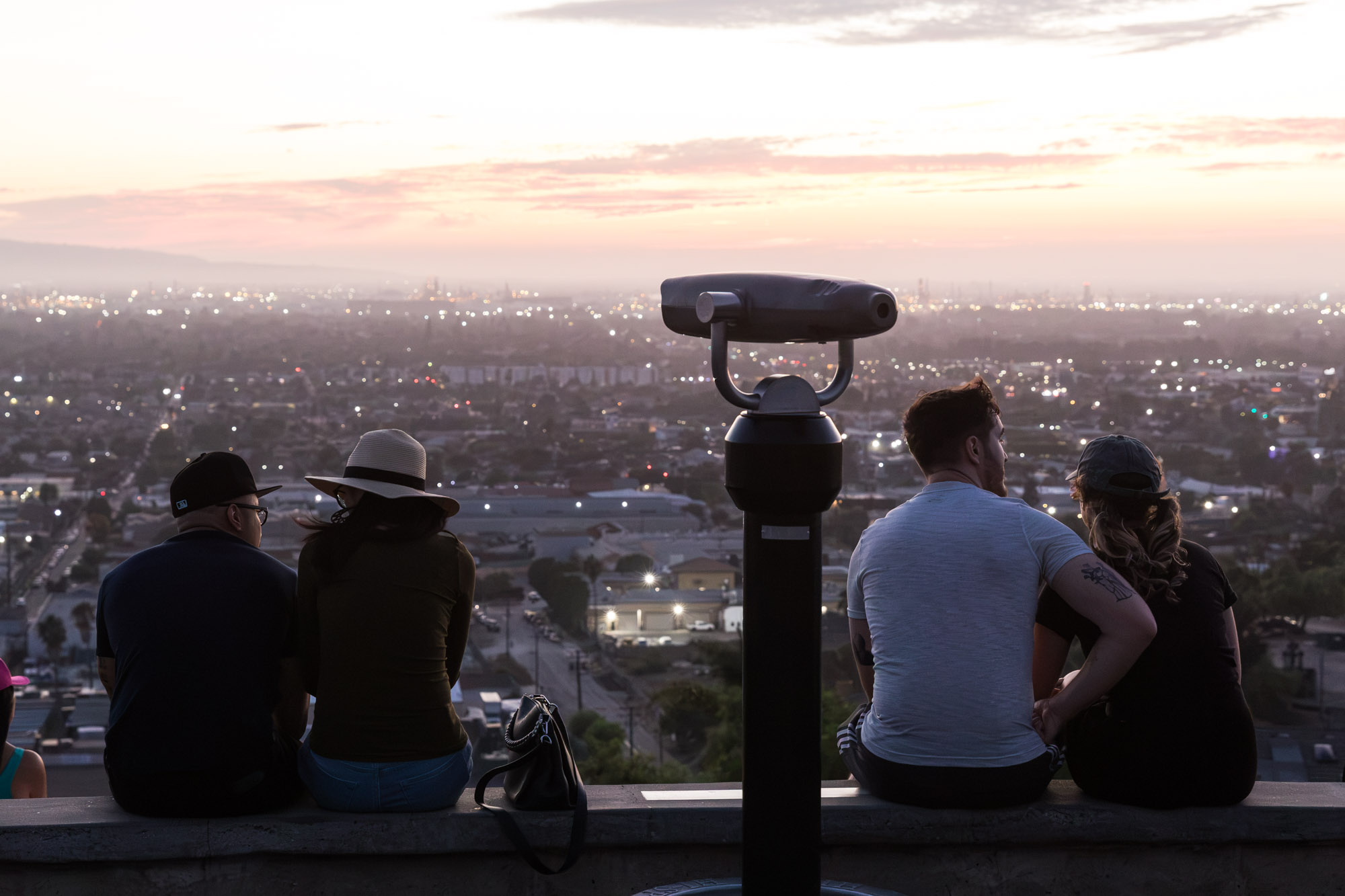 People sitting on a concrete curb at sunset in Hilltop Park with a standing binocular in the middle of the photo for an article on where to propose in Long Beach