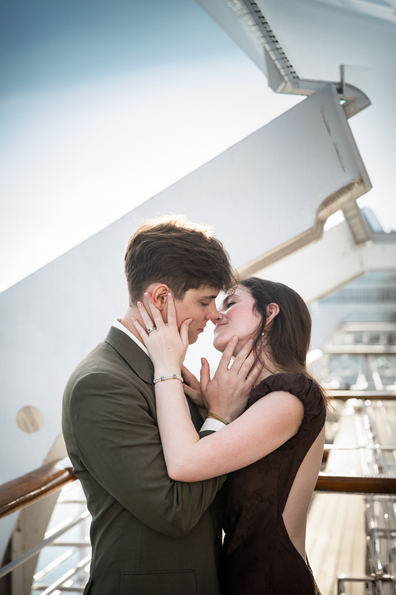 Couple cupping each other's faces for a near kiss against a white gantry on a Queen Mary photo shoot