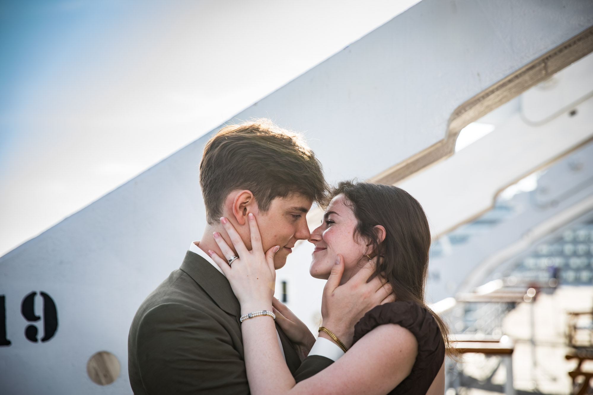 Couple nose to nose with their hands on each other's faces beside a numbered gantry, a romantic Queen Mary photo shoot portrait
