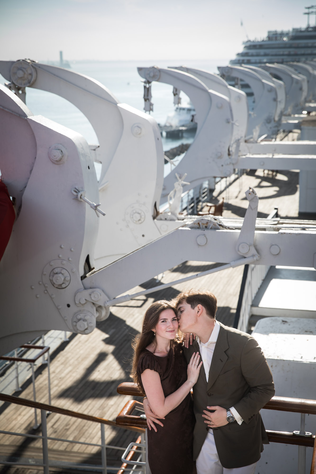 Man kissing the woman's cheek at the rail beneath rows of white gantries, photographed by a Long Beach photographer
