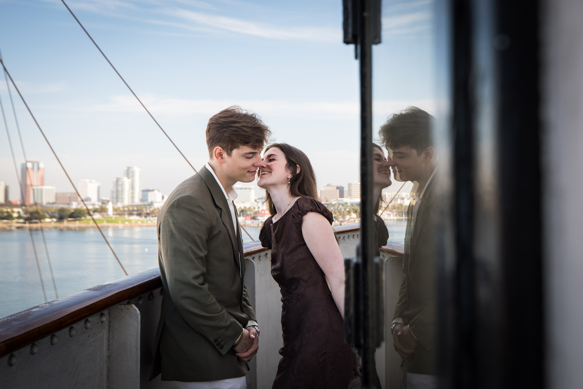 Woman smiling as she leans in for a kiss while the Long Beach skyline shows behind them, a Queen Mary photo shoot moment