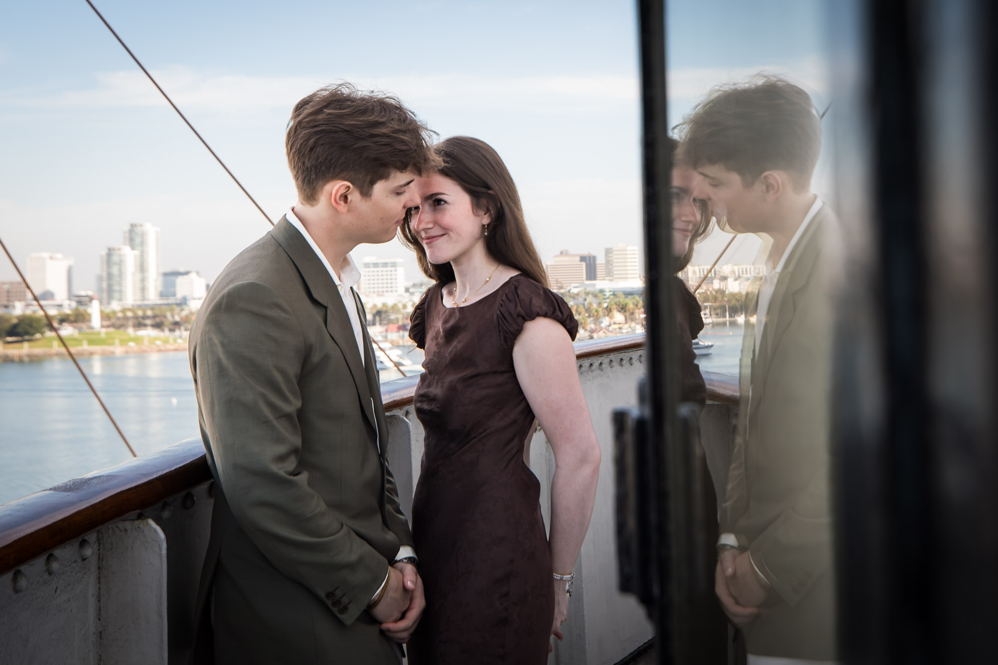 Couple nose to nose on the Bridge walkway with the Long Beach skyline behind them, during their Queen Mary photo shoot