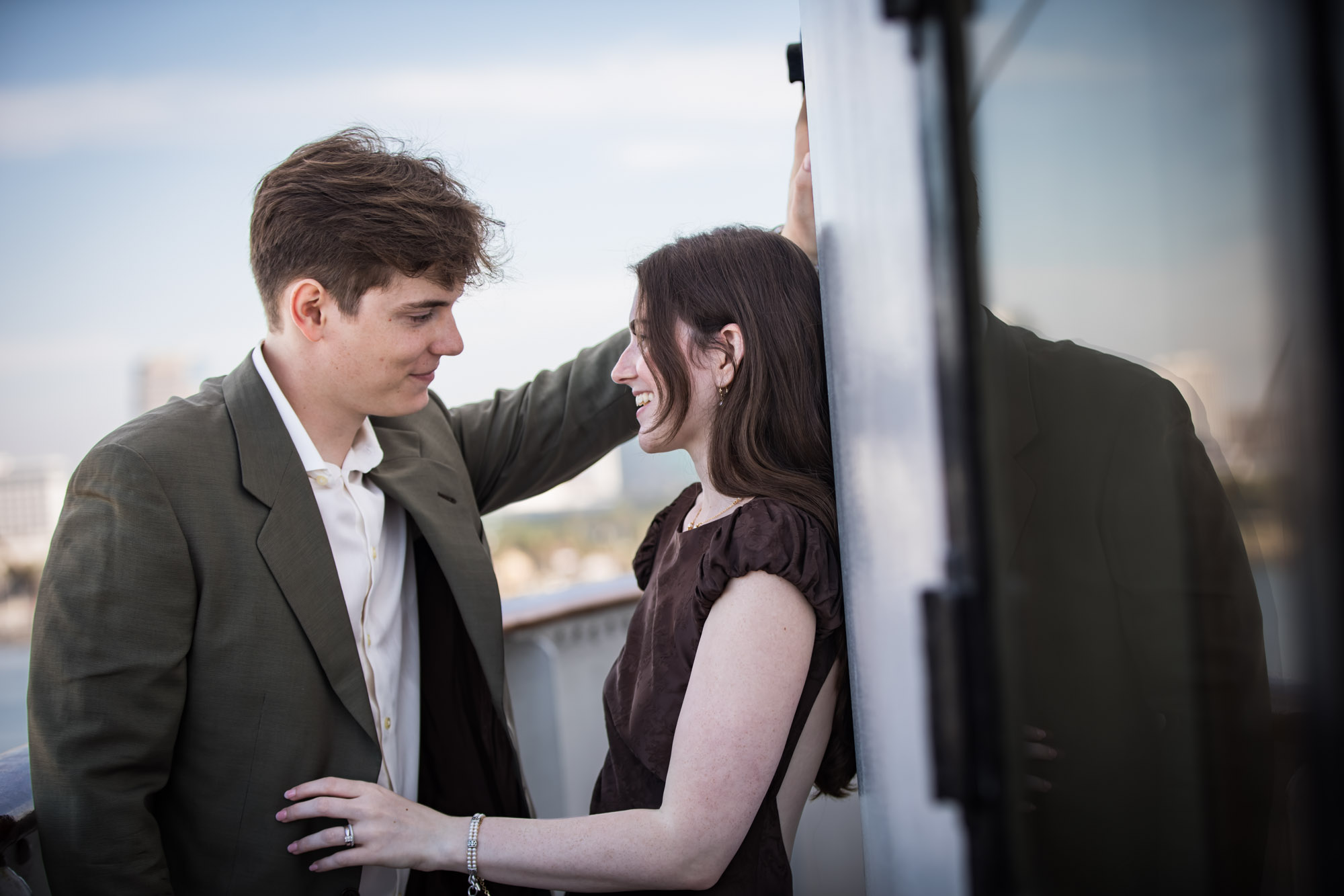 Woman laughing as the man smiles down at her beside the wheelhouse wall, a candid moment from their Queen Mary photo shoot