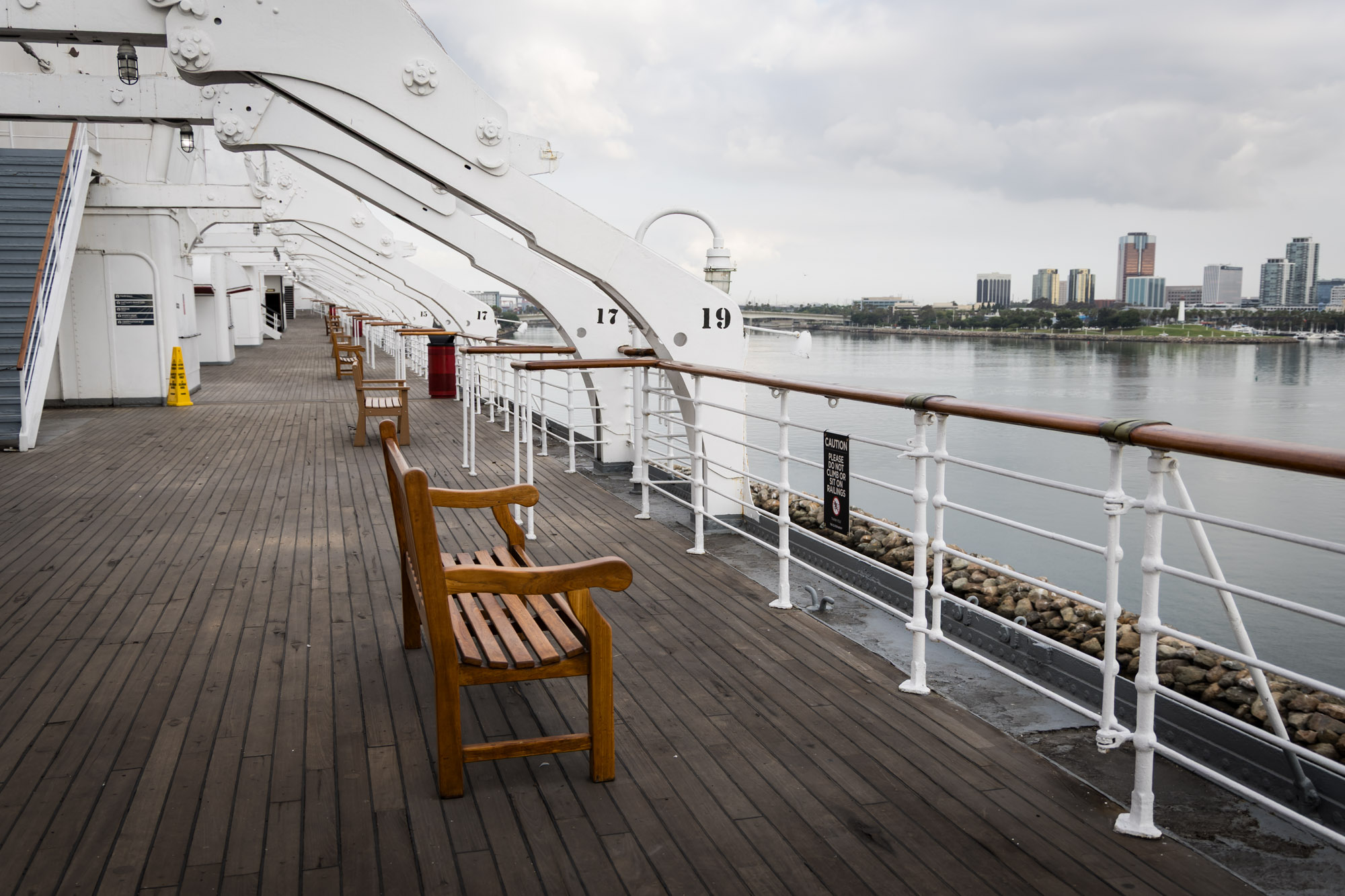 Wooden bench beneath numbered gantries with the Long Beach skyline across the water, a favorite Queen Mary photo shoot spot