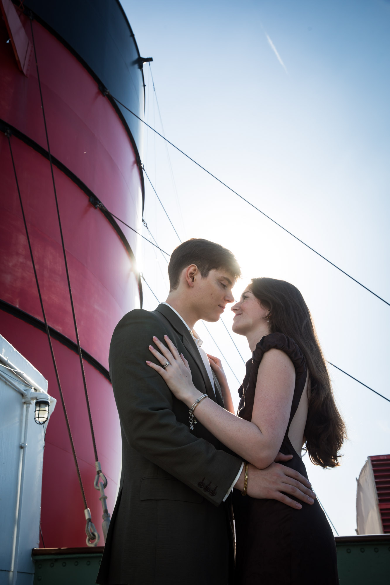 Low-angle, backlit engagement photo of a couple nearly kissing in front of a red funnel, a Queen Mary photo shoot highlight
