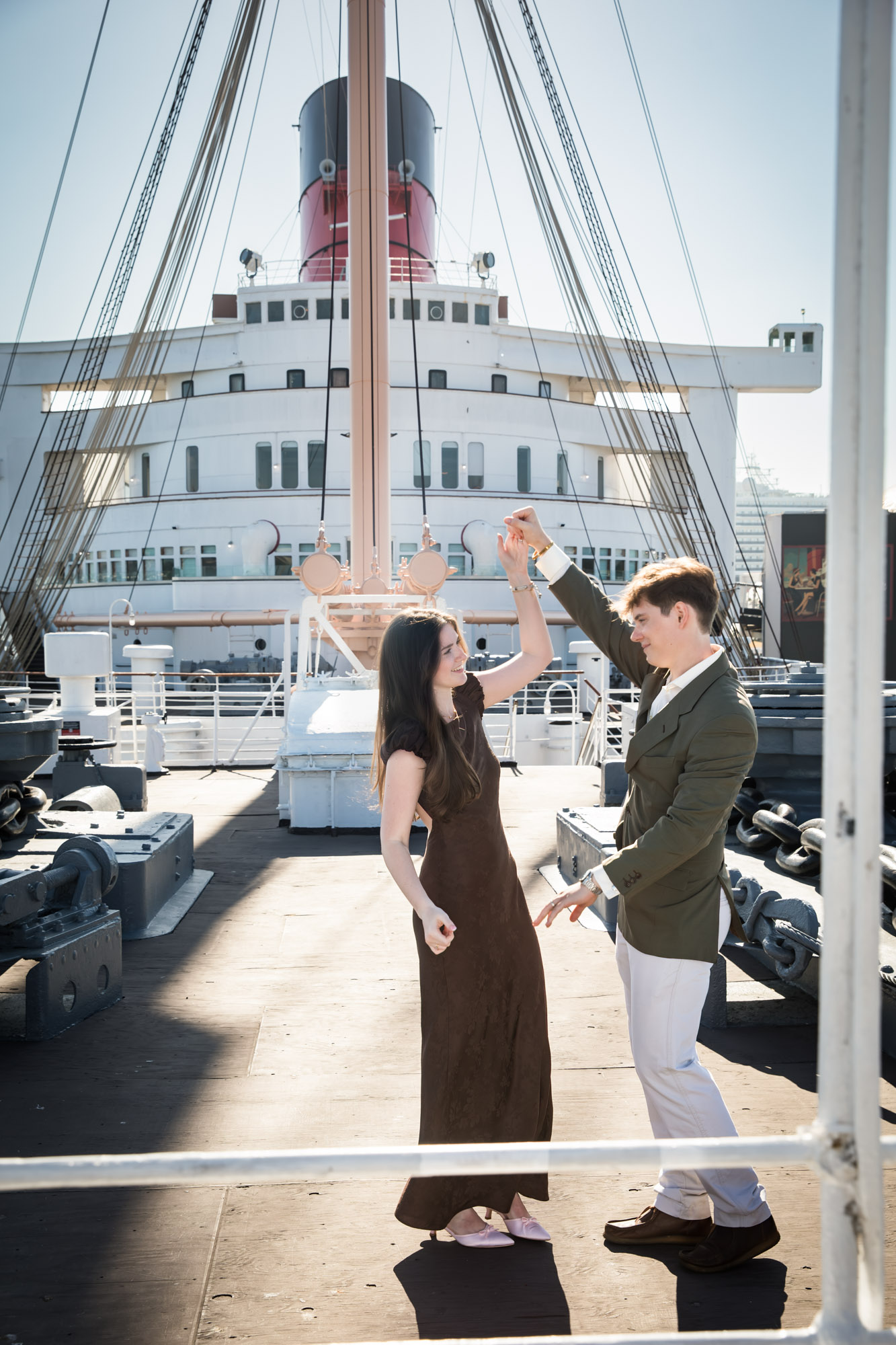 Woman twirling under her fiancé's arm on the ship's bow with the mast and funnel behind them, by a Los Angeles photographer