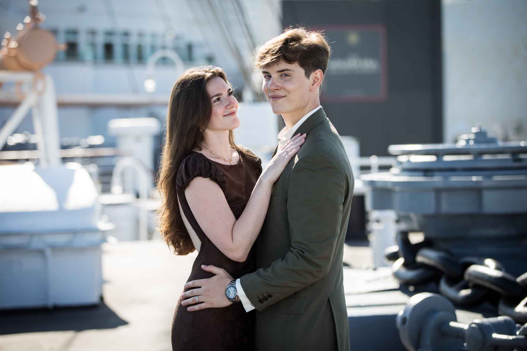 Man glancing at the camera while his fiancée gazes up at him on deck, Queen Mary photo shoot