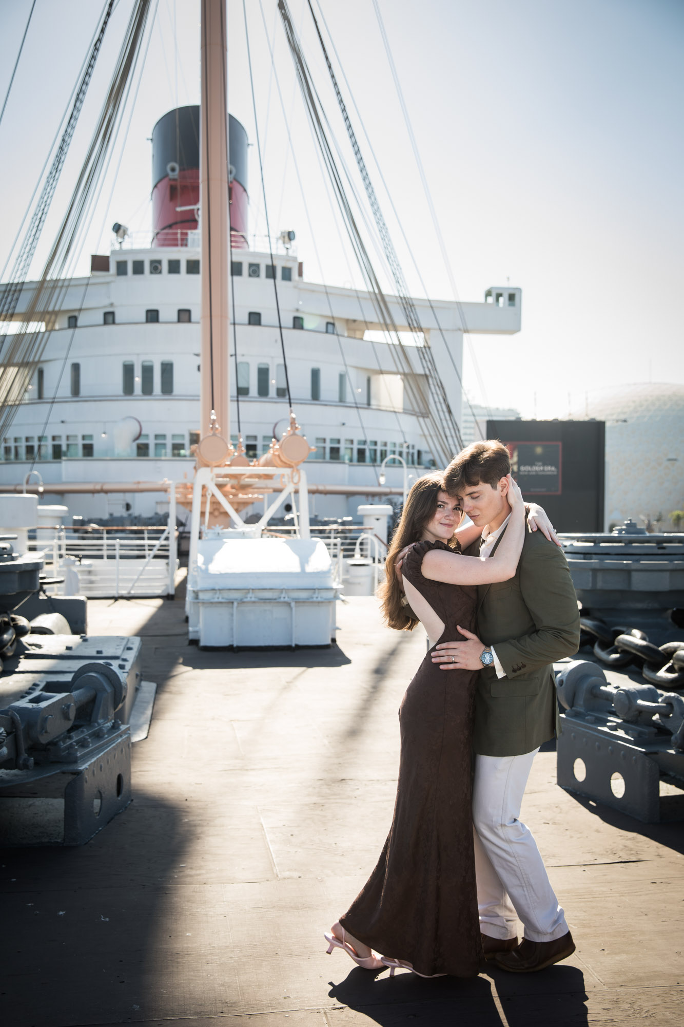 Couple dancing in a close embrace as she smiles at the camera, with the full ship behind them, Queen Mary photo shoot