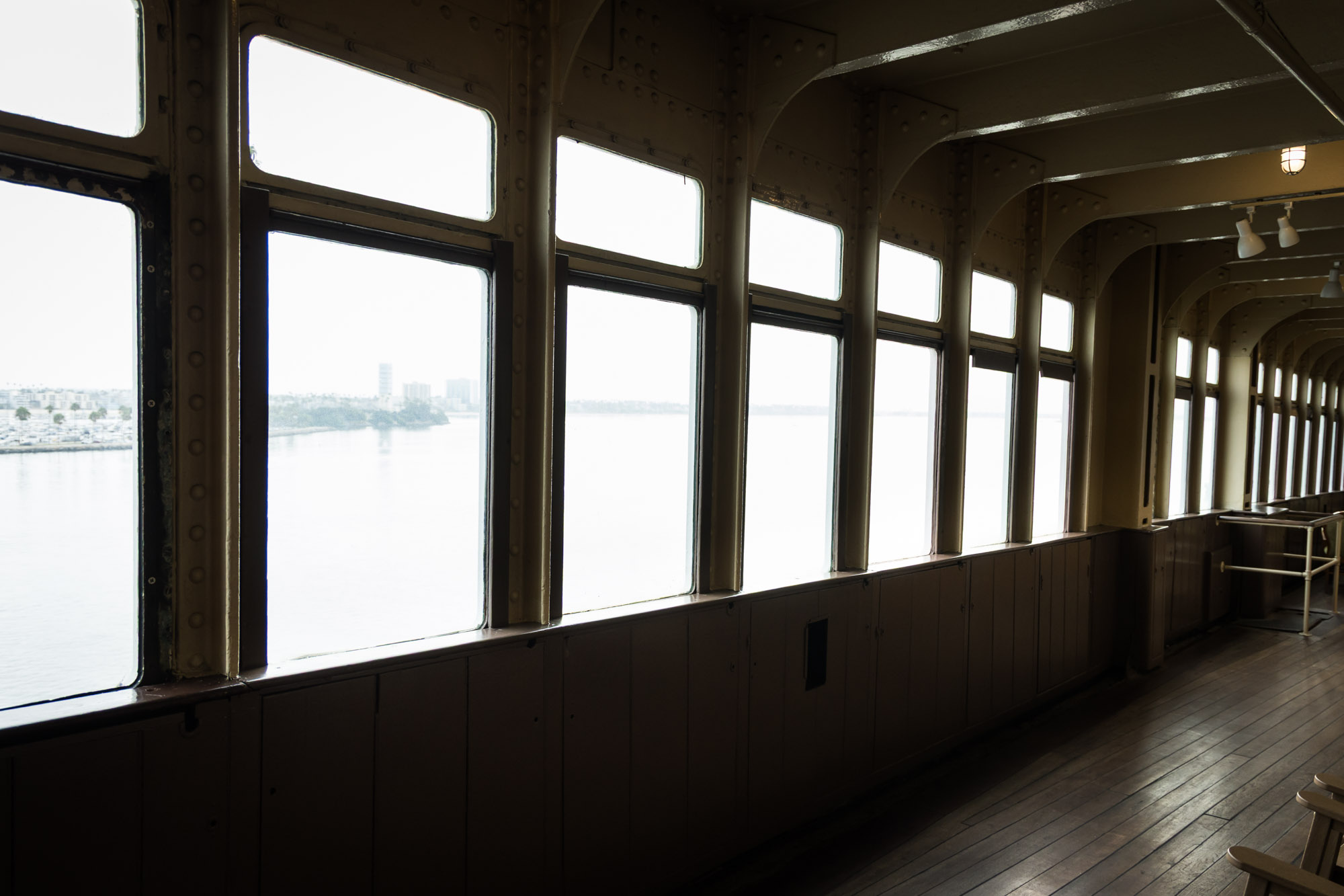 Los Angeles photographer's view of tall windows overlooking the harbor along a wood-floored enclosed deck on the Queen Mary