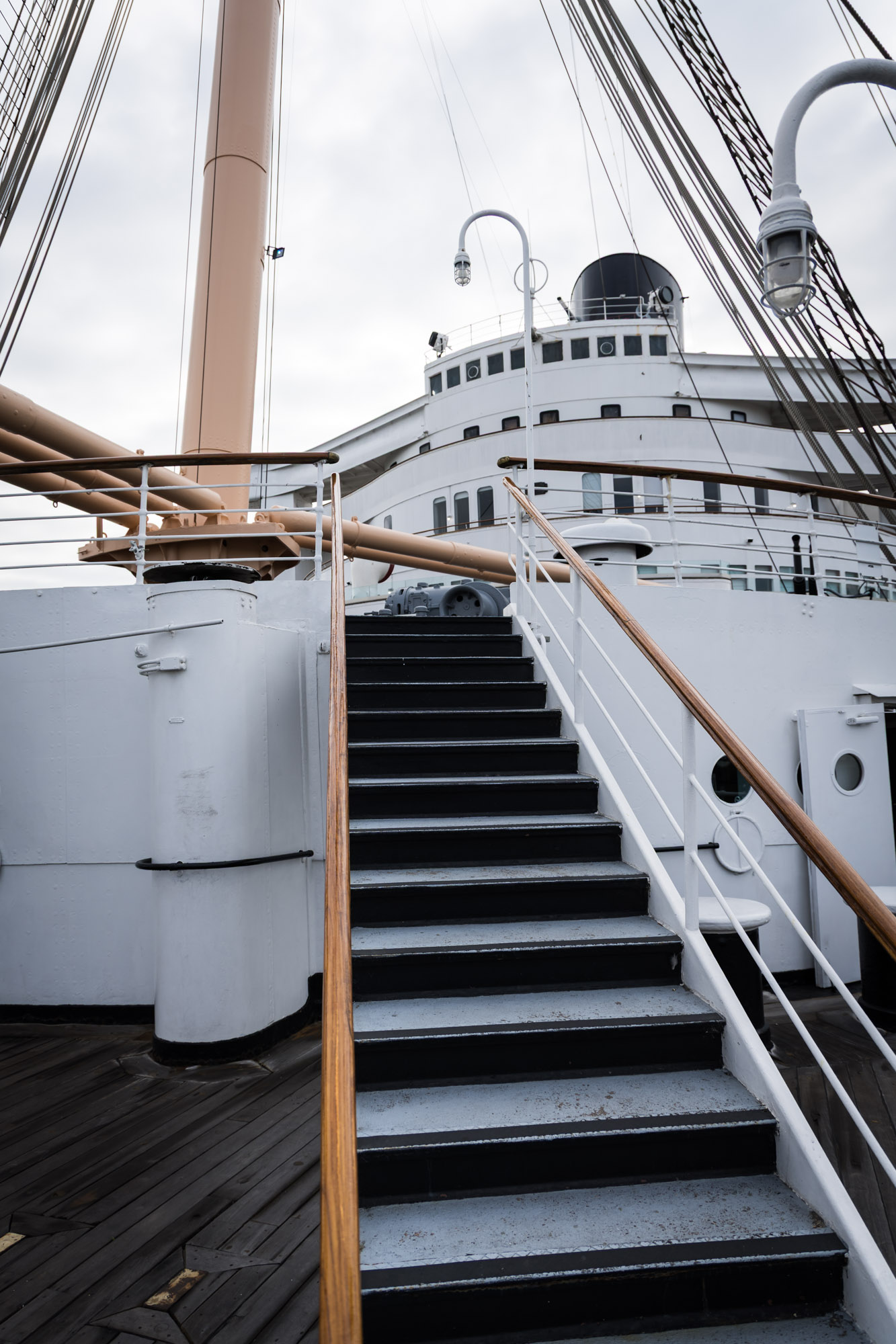 Long Beach photographer's view of a wood-railed staircase leading up toward the Queen Mary bow, with mast and rigging overhead
