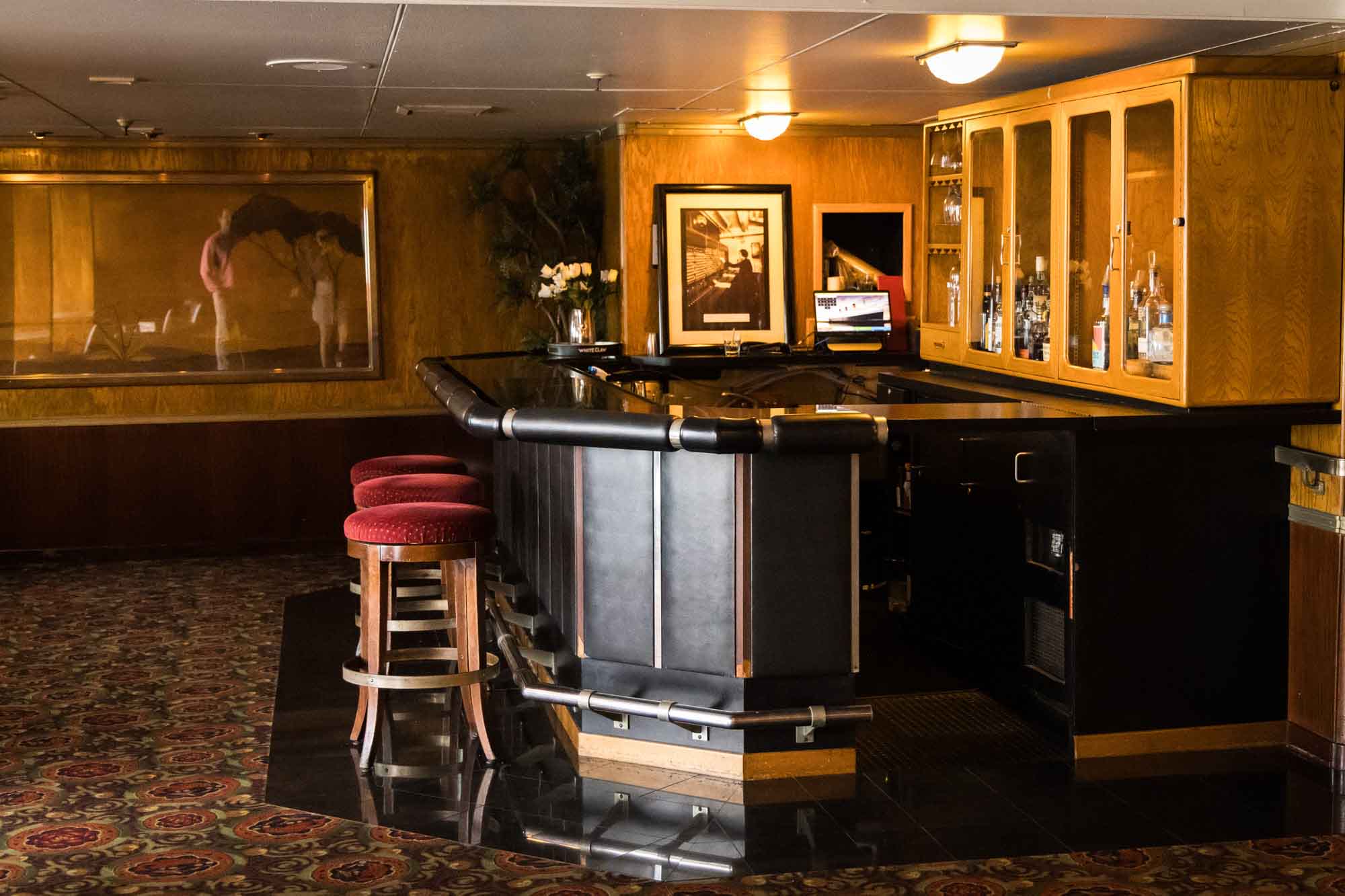 Art deco bar with red upholstered stools and glass-front cabinets, an interior stop on a Queen Mary photo shoot