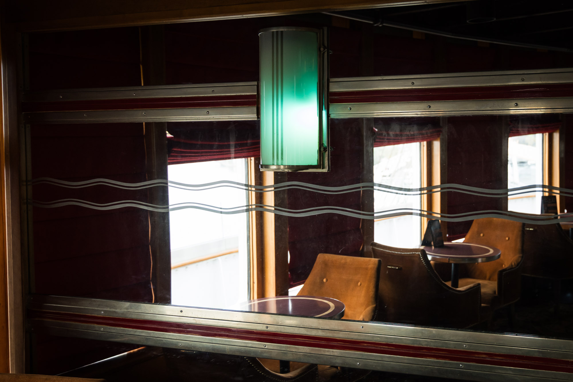Etched mirror and green art deco lamp reflecting leather armchairs and a window, an interior detail for a Queen Mary photo shoot