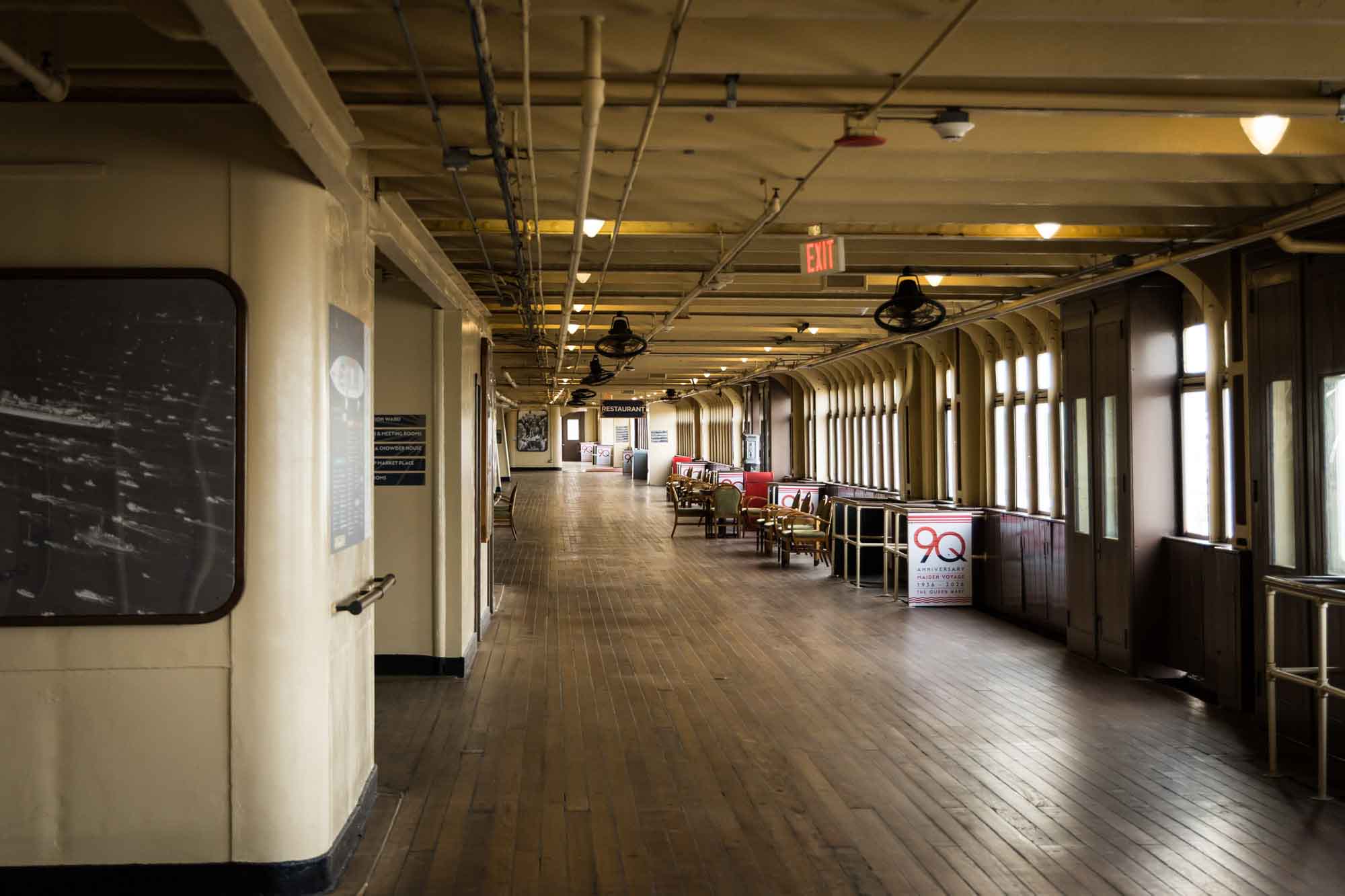 Long Beach photographer's view of a long wood-floored interior Promenade Deck lined with windows and chairs on the Queen Mary