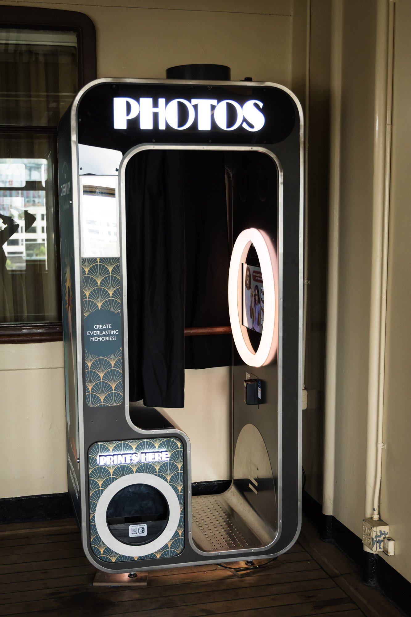 Art deco photo booth with a lit "PHOTOS" sign and ring light, a fun stop on a Queen Mary photo shoot