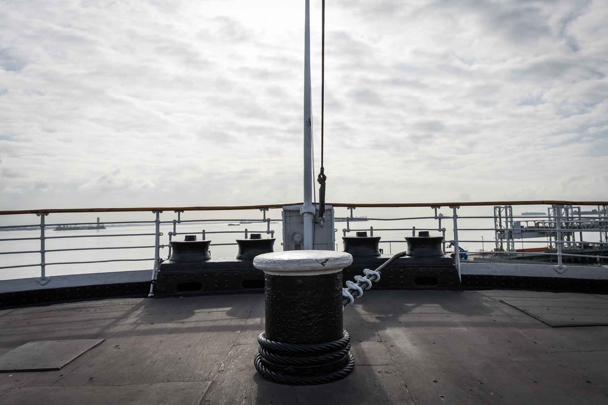 Los Angeles photographer's view of a black mooring bollard with coiled wire rope on the bow deck, with a flagpole and harbor railing behind