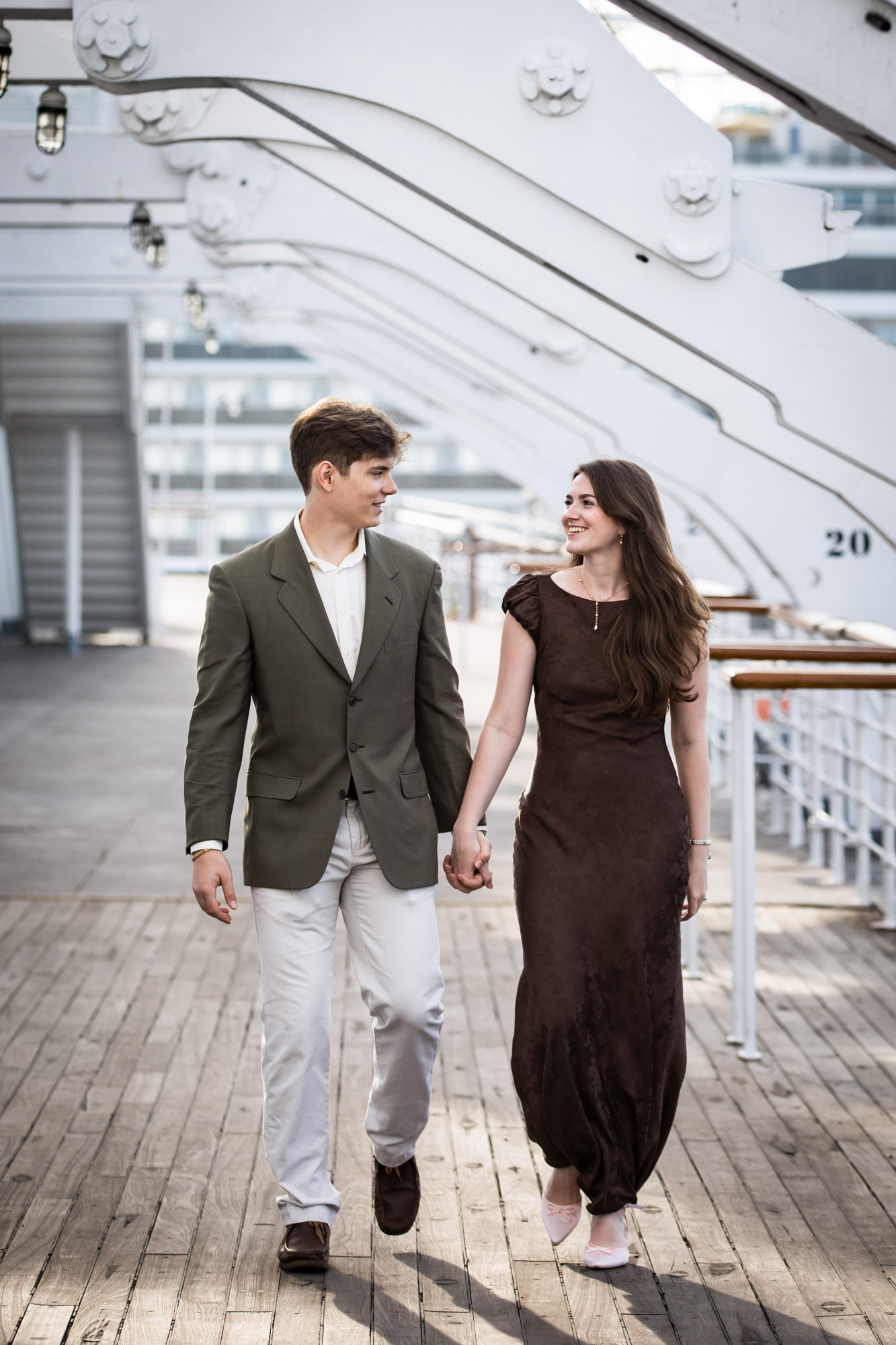 Couple walking hand in hand along the Sun Deck beneath white gantries during their Queen Mary photo shoot