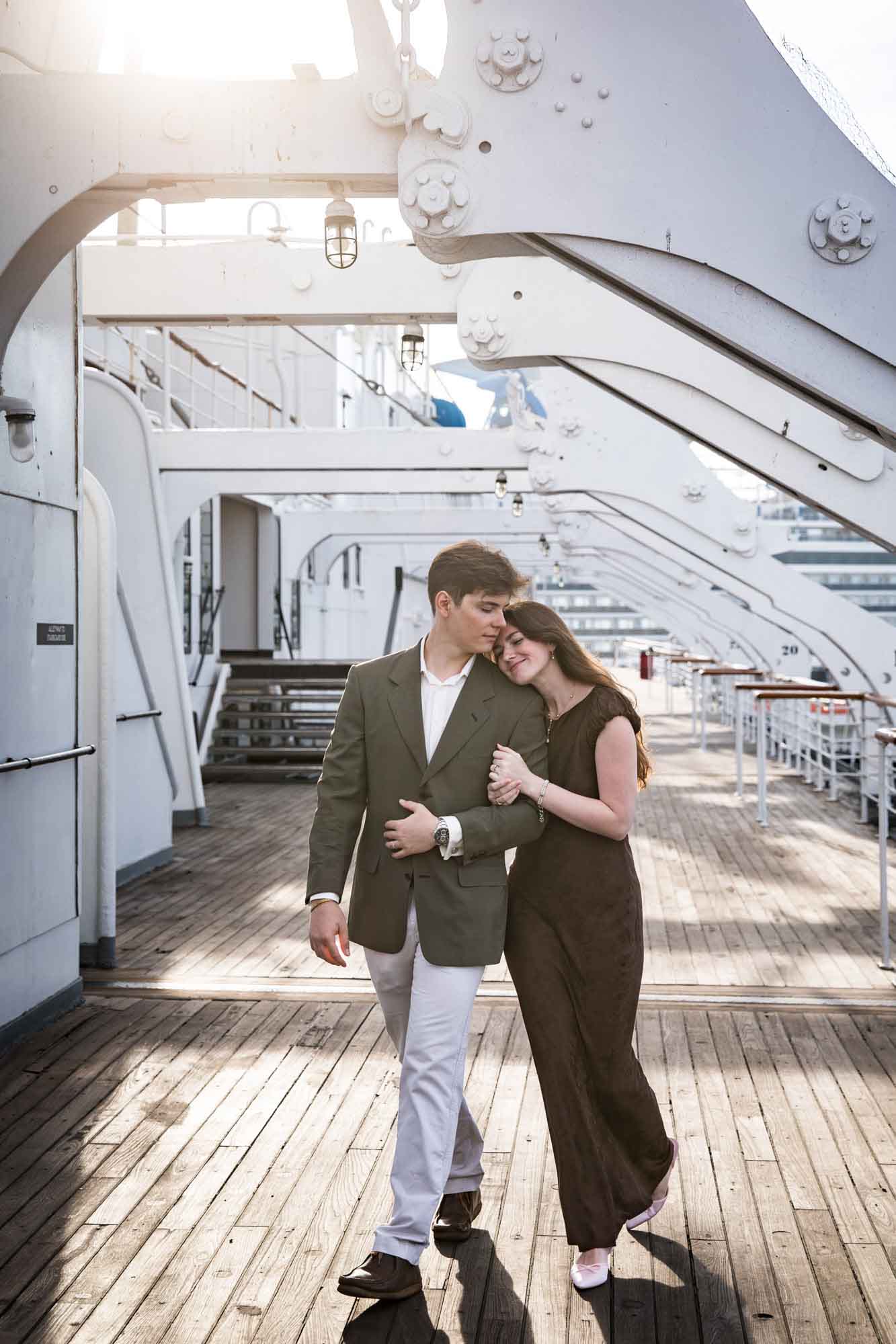 Woman resting her head on the man's shoulder as they walk arm in arm, sun flaring through the gantries on their Queen Mary photo shoot