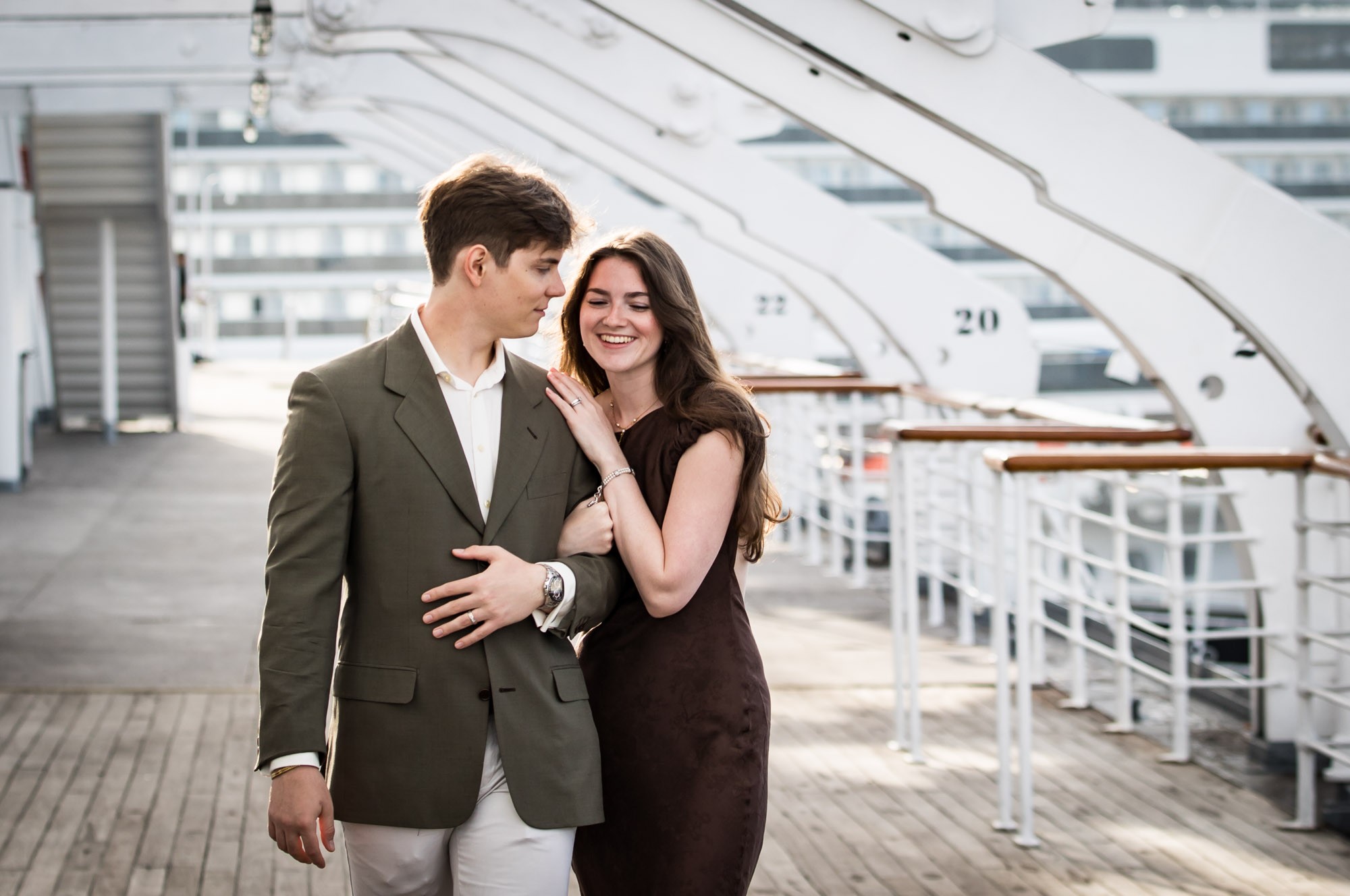 Woman laughing with her eyes closed as she holds the man's arm while he looks at her, a candid moment from a Queen Mary photo shoot