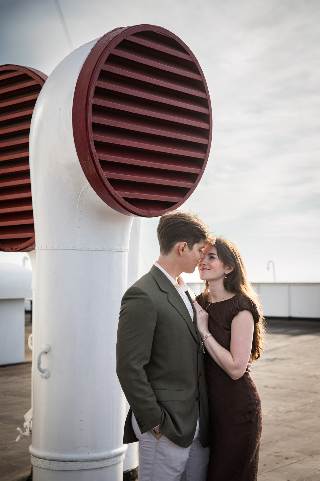 Couple embracing beside a white ventilator with a red louvered cowl during a Queen Mary photo shoot