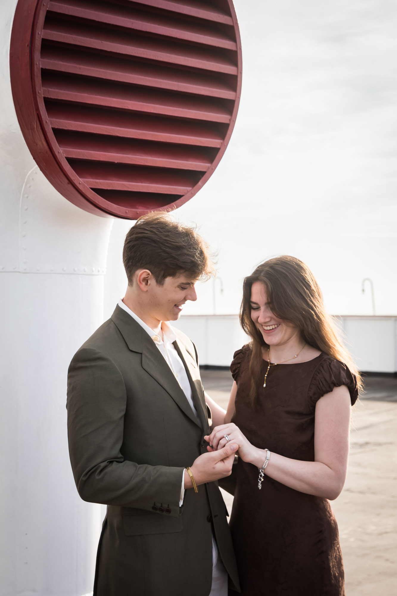 Couple laughing as they look at her ring while holding hands on a Queen Mary photo shoot