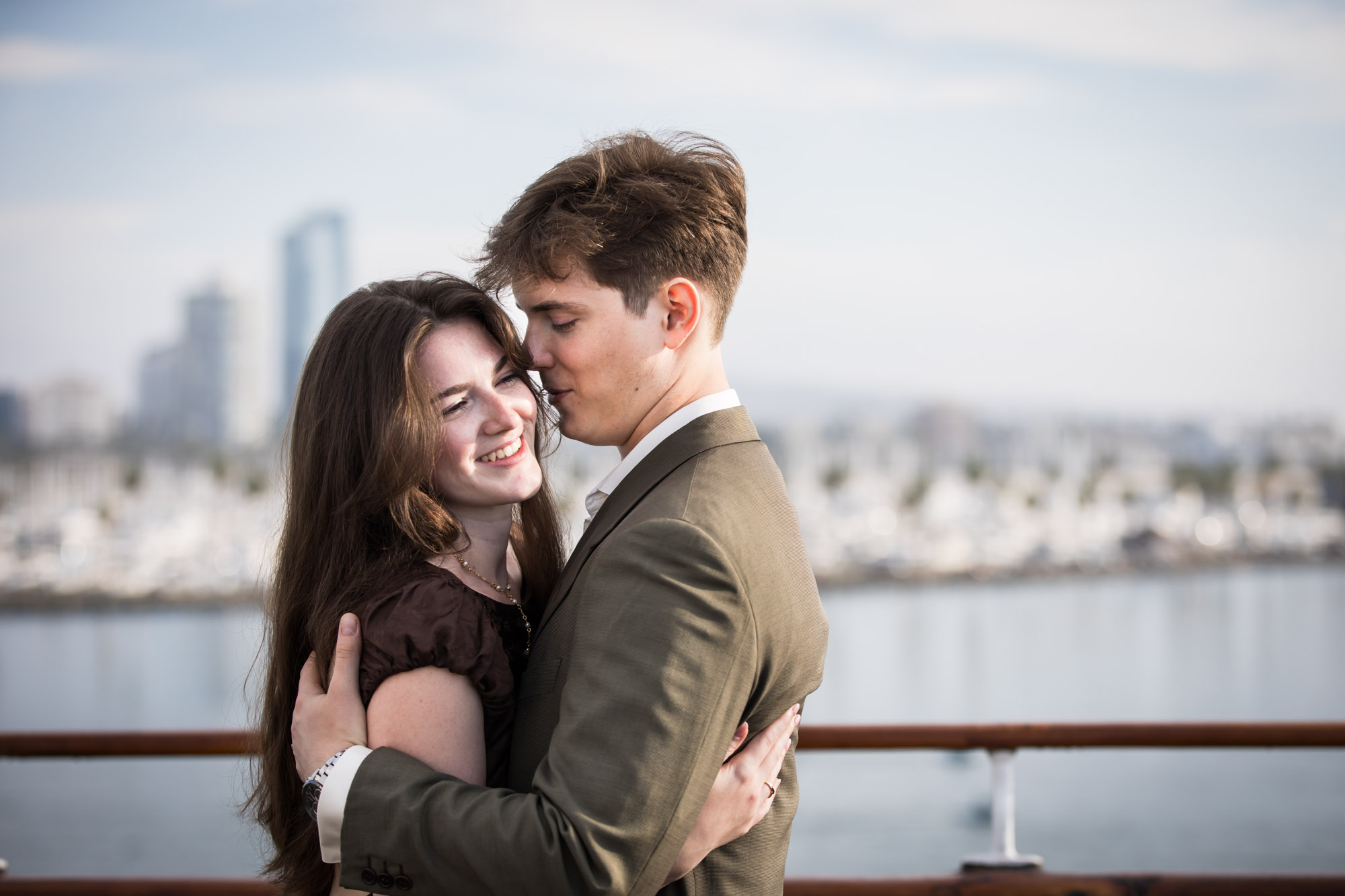 Man kissing the woman's temple as she laughs at the rail, photographed by a Long Beach photographer