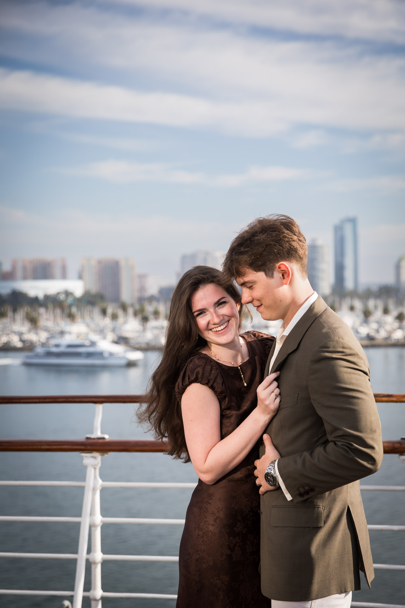 Woman laughing with her hand on the man's lapel as a yacht passes in the harbor, photographed by a Los Angeles photographer